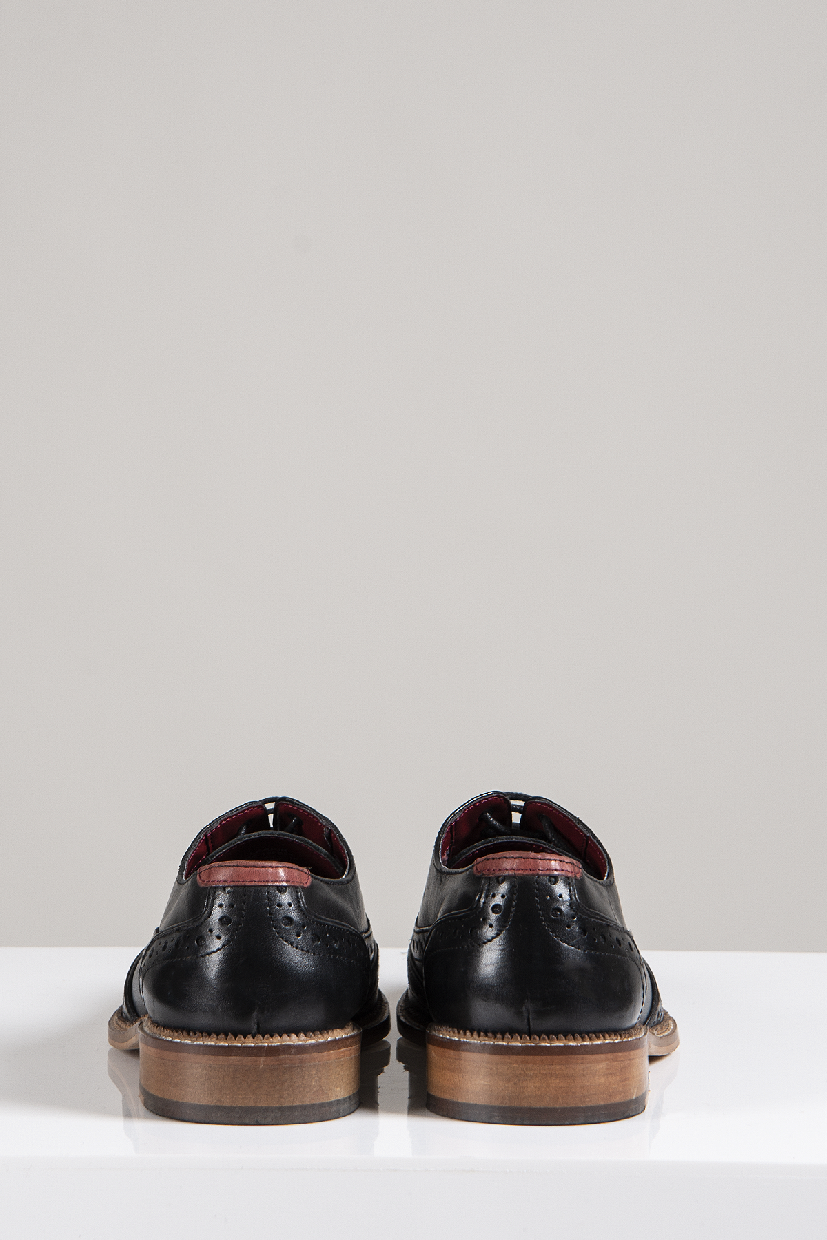 The Marc Darcy LARKIN Black Leather Brogue Shoes feature full grain leather and brown soles, displayed from the back on a white surface with a plain light gray background.