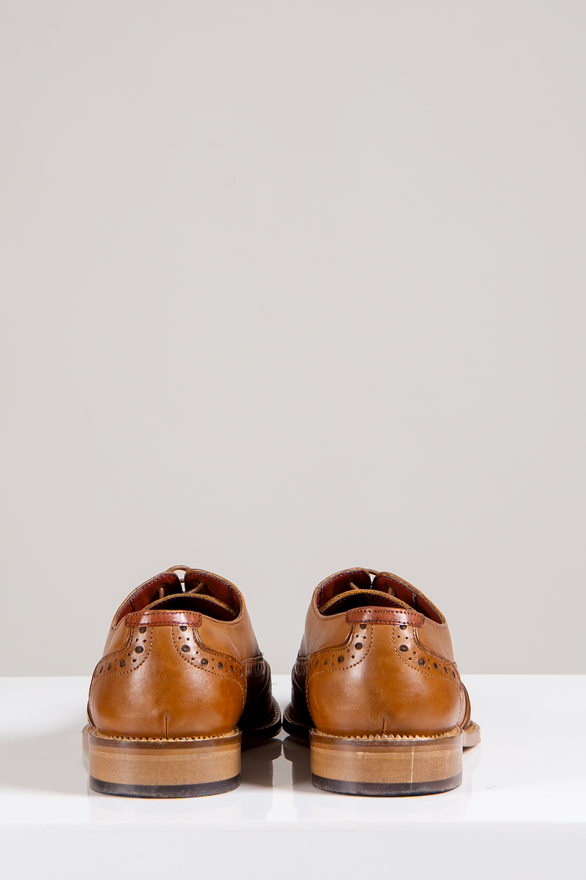 The Marc Darcy LARKIN Mid Tan Leather Brogue Shoes, made from full grain leather, are seen from the back on a white surface with a plain gray background.
