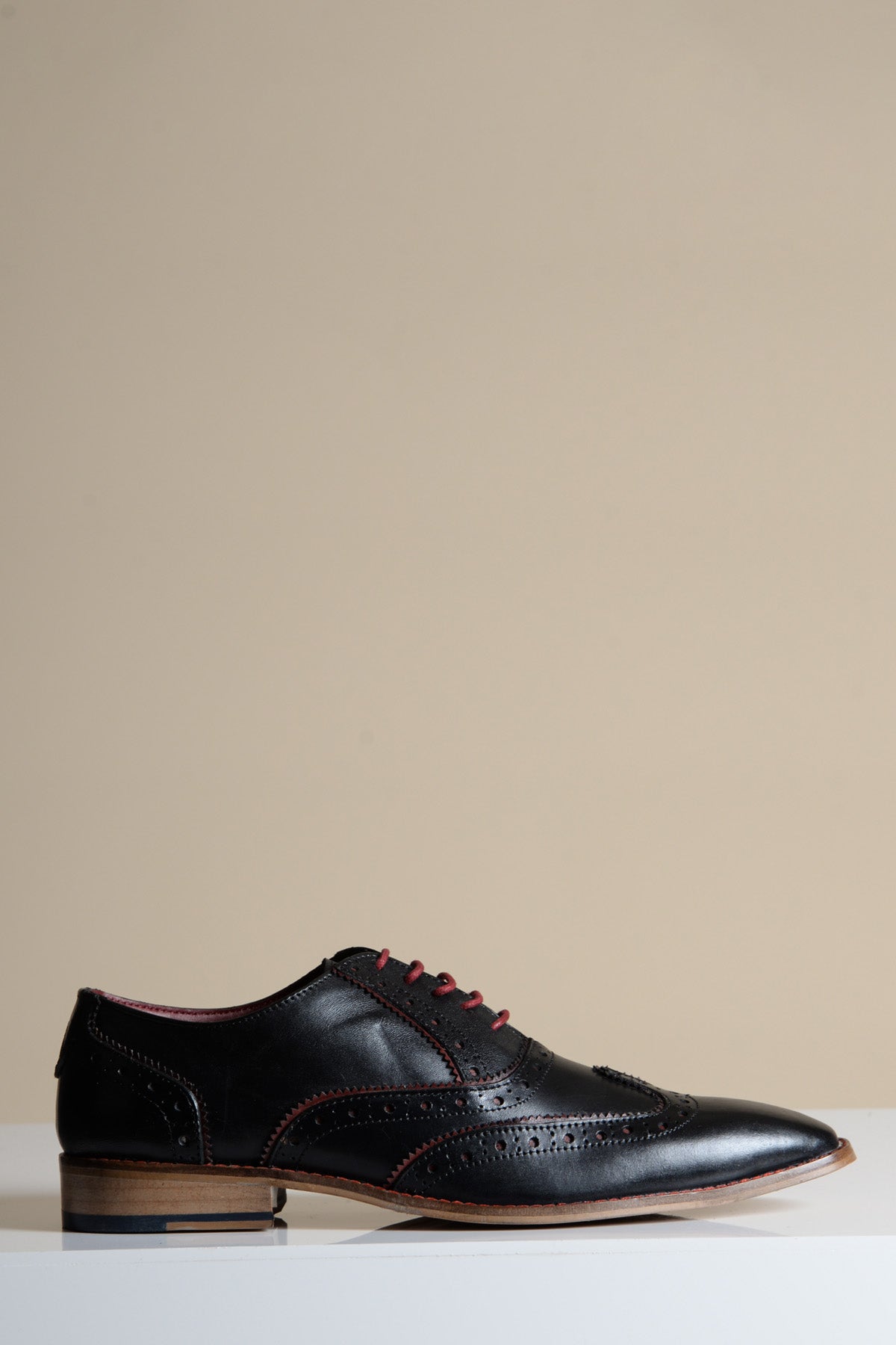 The MARCO by Marc Darcy is a black Bordeaux leather wingtip oxford shoe with decorative stitching, red laces, and a wooden sole, shown against a plain beige background.