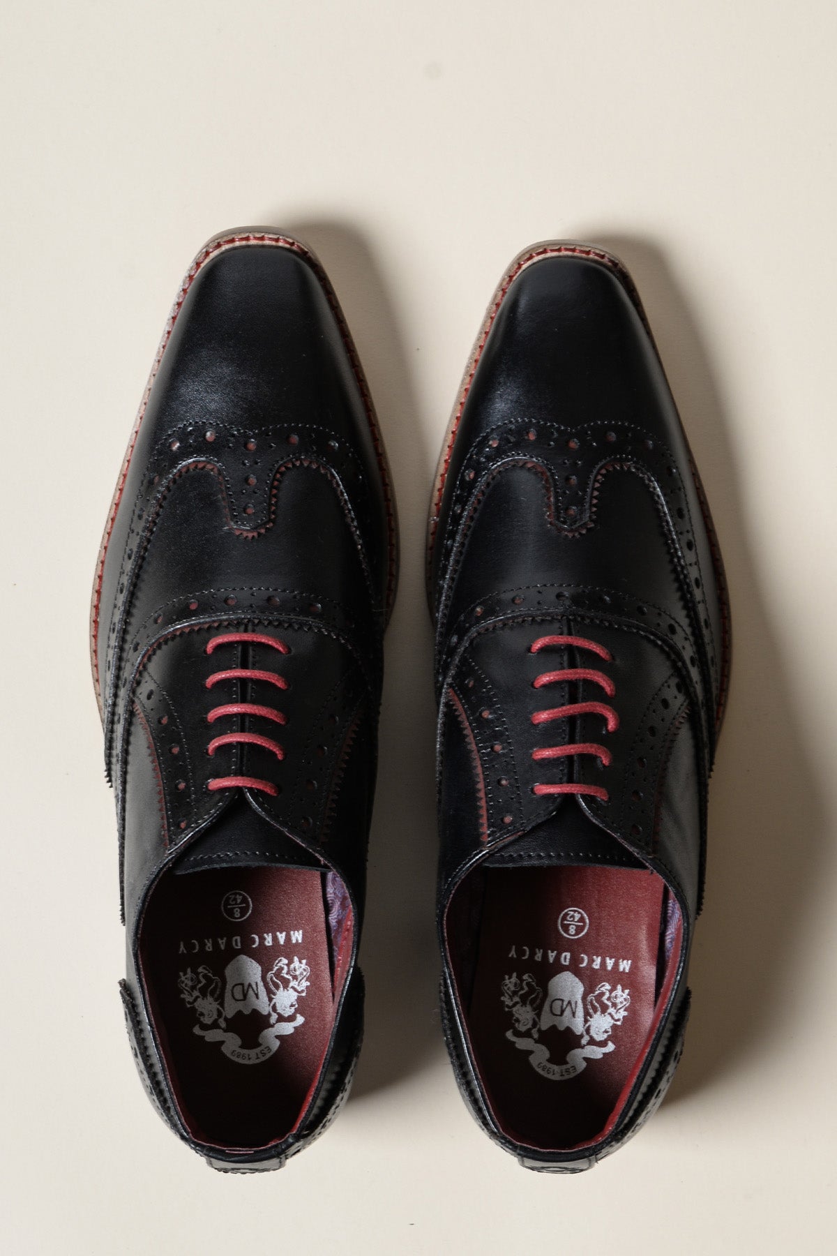 The MARCO Black Bordeaux Leather Wingtip Oxford Shoes by Marc Darcy, featuring pink laces and burgundy interiors, are crafted from full grain leather and displayed side by side on a light-colored surface.