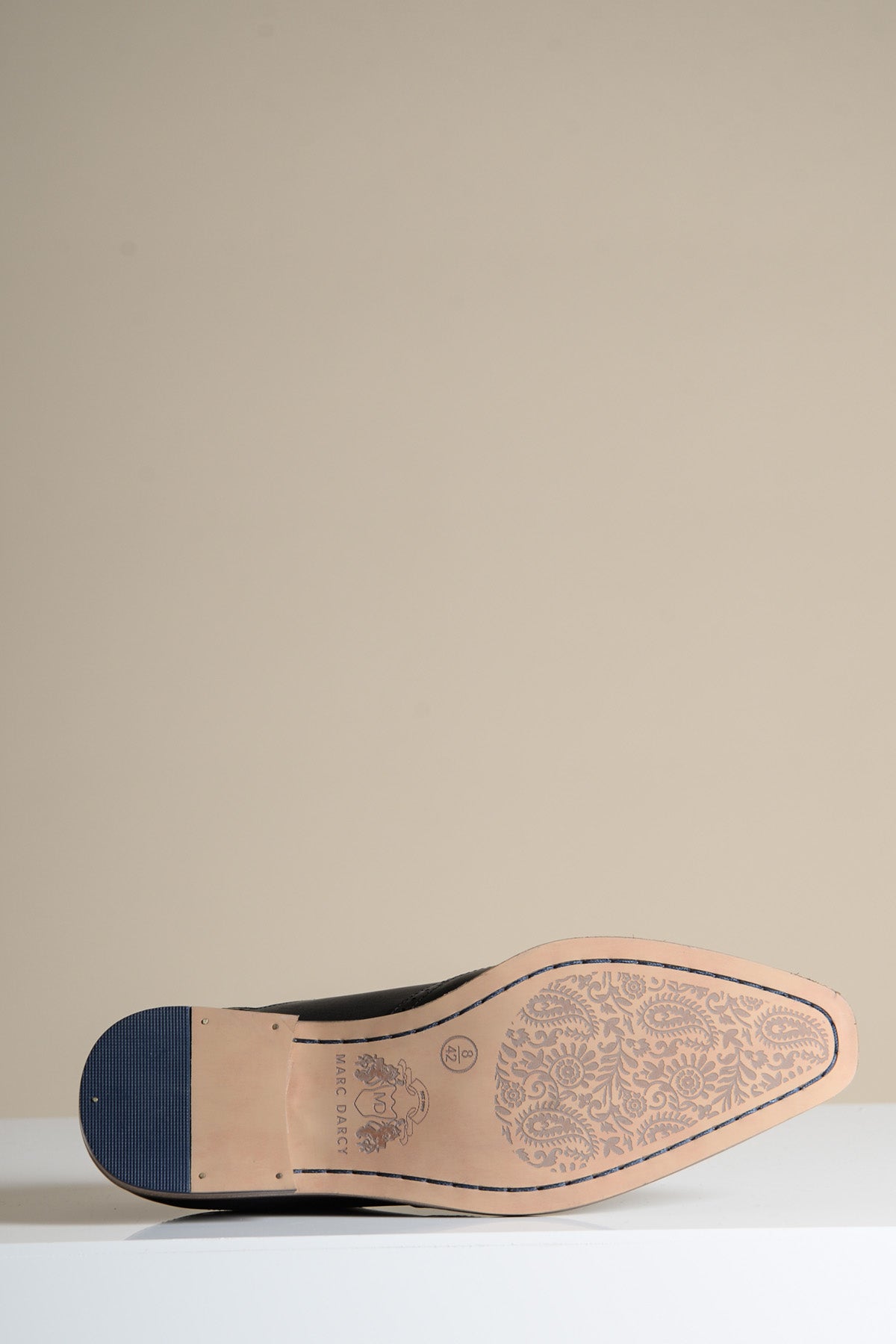 The Marc Darcy DAWSON Black Wingtip Oxford Brogue Shoe is shown sole-up on a white surface, highlighting its beige floral-patterned sole and blue heel cap—ideal for those who appreciate full grain leather craftsmanship.