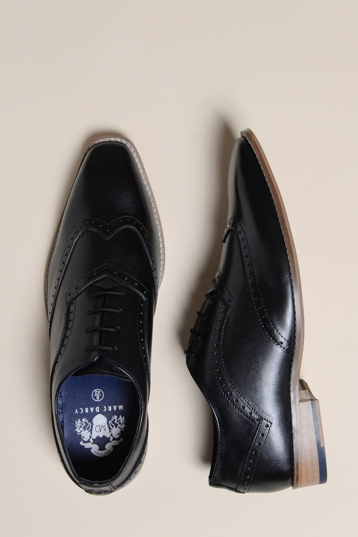 The DAWSON - Black Wingtip Oxford Brogue Shoe by Marc Darcy, crafted from full grain leather with brogue detailing, lace-up fronts, and wooden heels, is displayed on a beige background—one top-down, one side view.