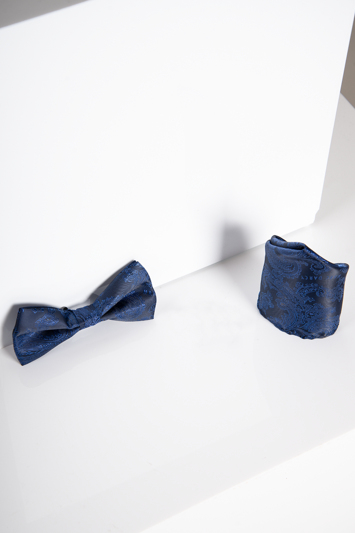 The MD PAISLEY - Navy Paisley Bow Tie and Pocket Square Set by Accessory, featuring a pre-tied bow tie and matching pocket square, is displayed on a white surface with a white background.