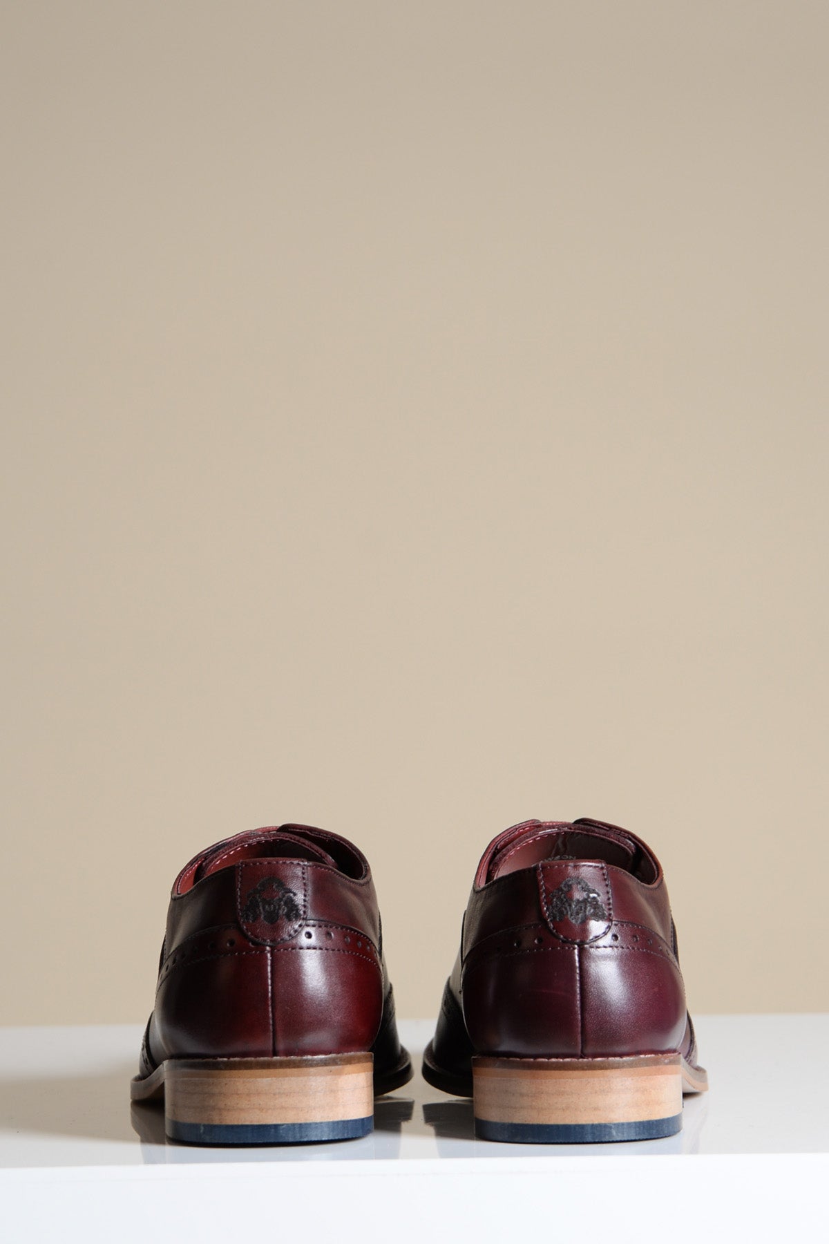 The Marc Darcy DAWSON Bordeaux Burgundy Wingtip Oxford Brogue Shoes, crafted from full grain leather, are shown from the back on a white surface with tan wooden heels and a light beige background.