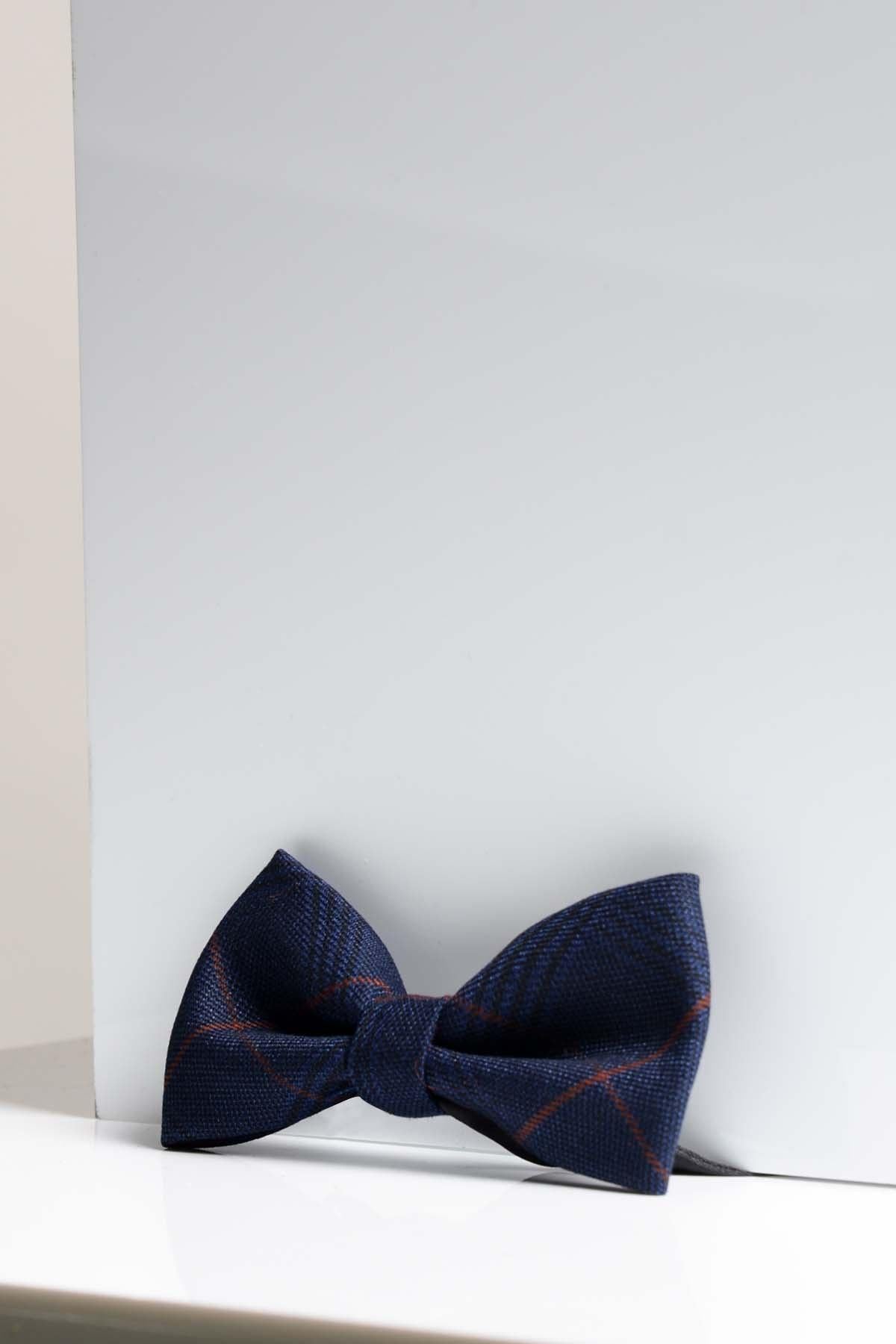 The EDINSON - Navy Wine Check Bow Tie by Accessory, featuring a subtle check pattern, is displayed on a white background near the corner of a reflective white surface.