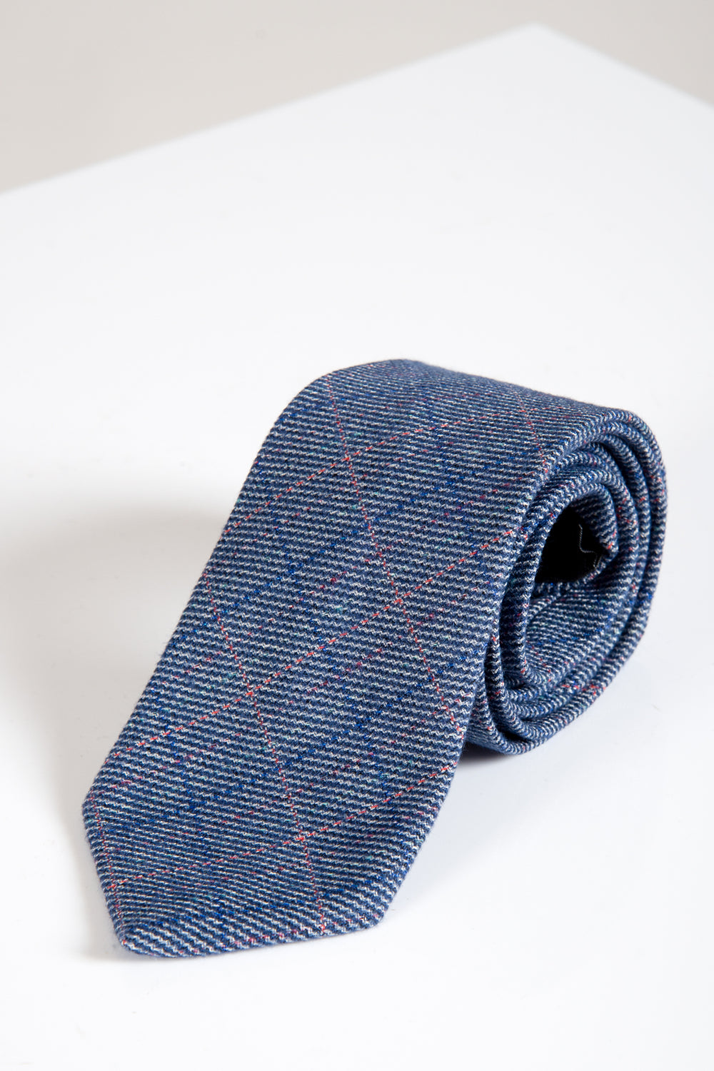 The HILTON Blue Check Tweed Tie by Accessory is a men’s dark blue necktie featuring a subtle plaid of thin red and white lines, shown rolled up on a white background with a soft shadow.