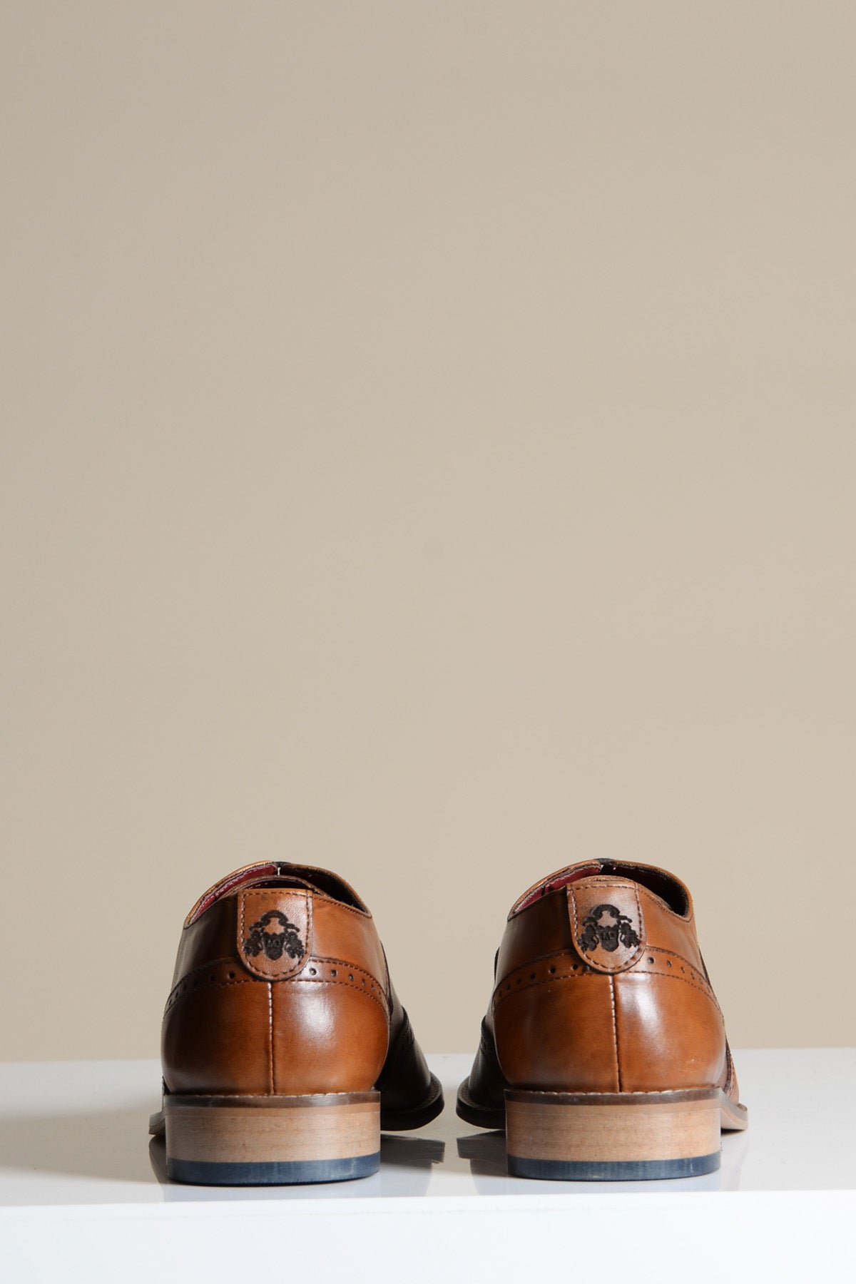 Two Marc Darcy DAWSON Tan Wingtip Oxford Brogue shoes, crafted from full grain leather with decorative broguing and a branded emblem on the heel, are viewed from the back.