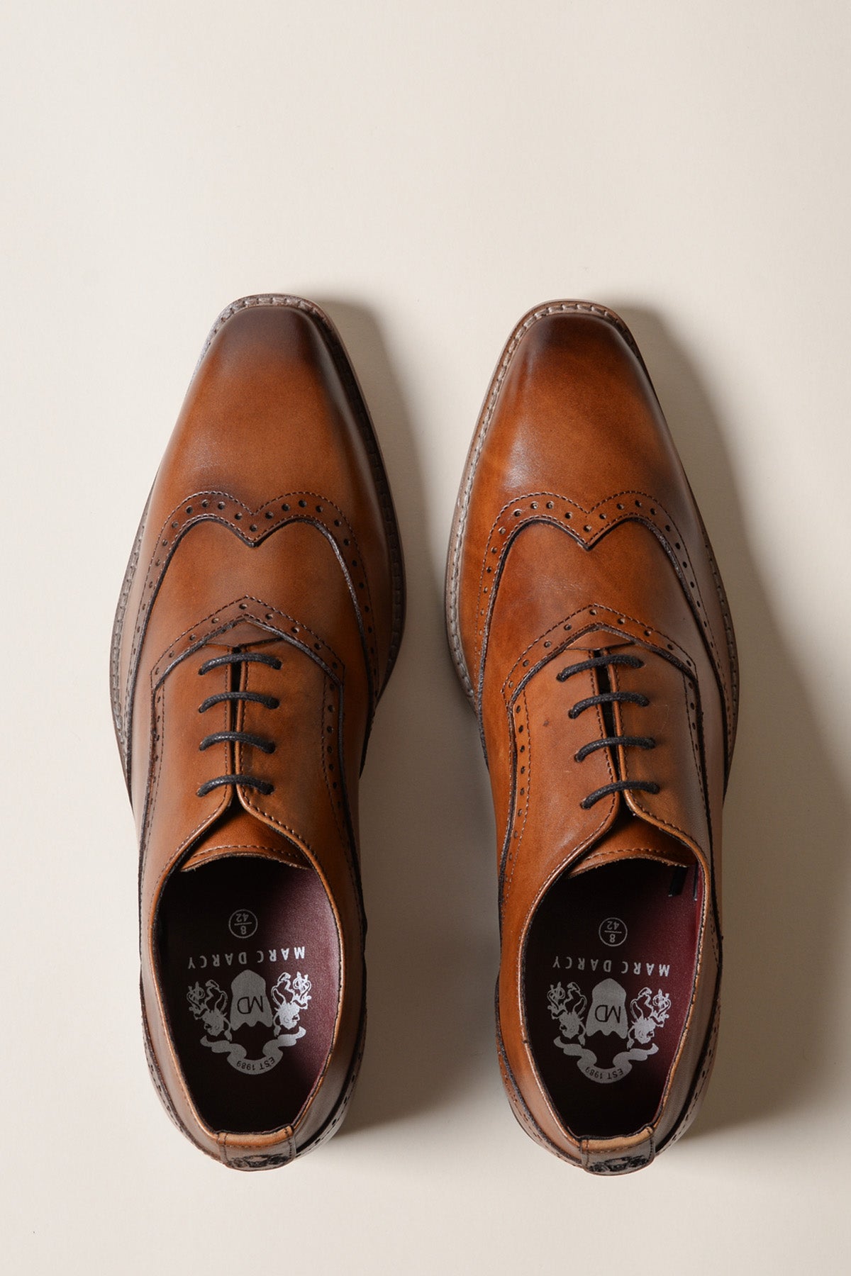 The DAWSON - Tan Wingtip Oxford Brogue Shoe by Marc Darcy is shown from above on a light background, featuring hand-stitched detailing. One shoe is neatly laced, while the other’s laces are loose and uneven.