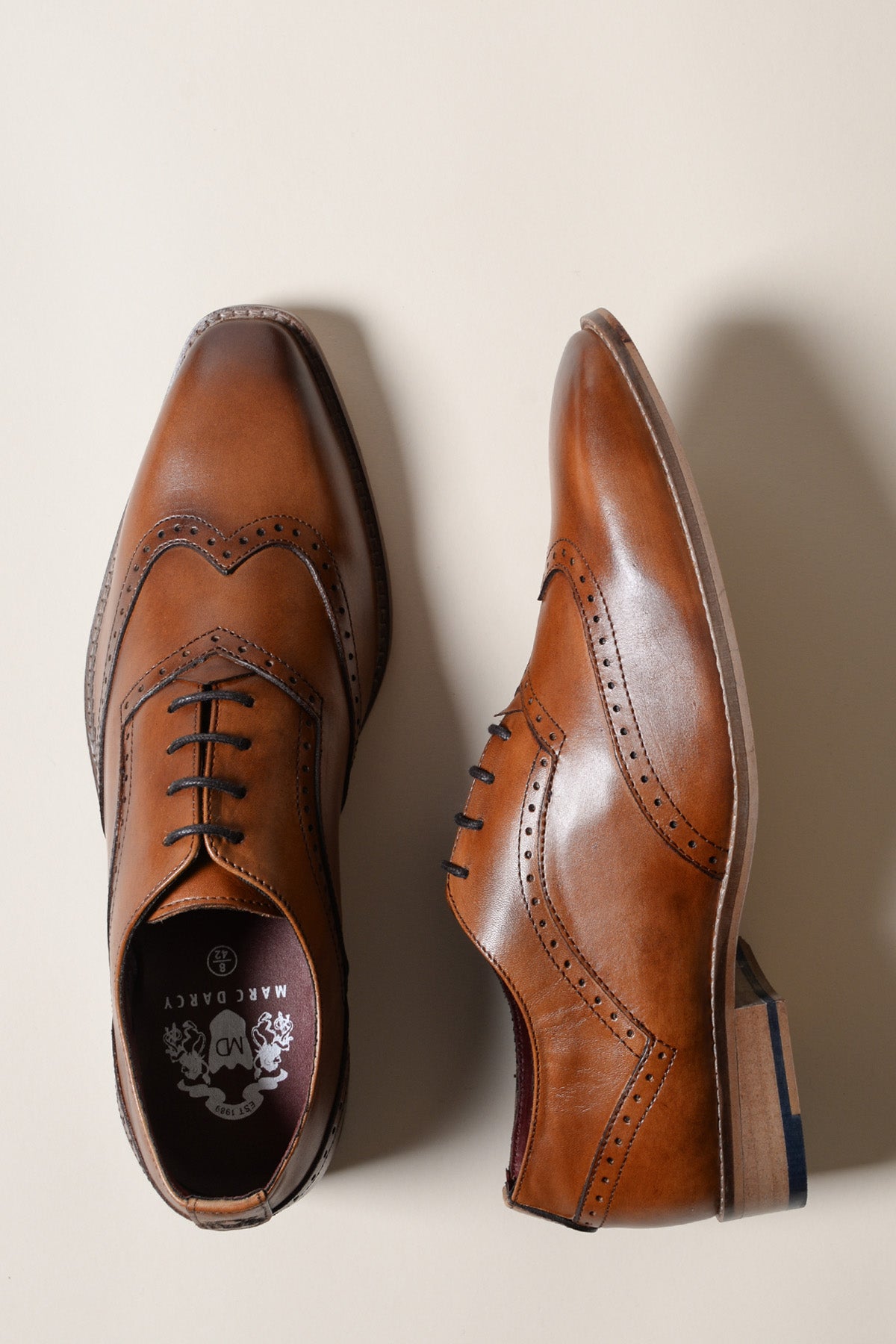 The Marc Darcy DAWSON tan wingtip oxford brogue shoes are shown from the top and side against a light beige background, highlighting their decorative detailing and classic style.