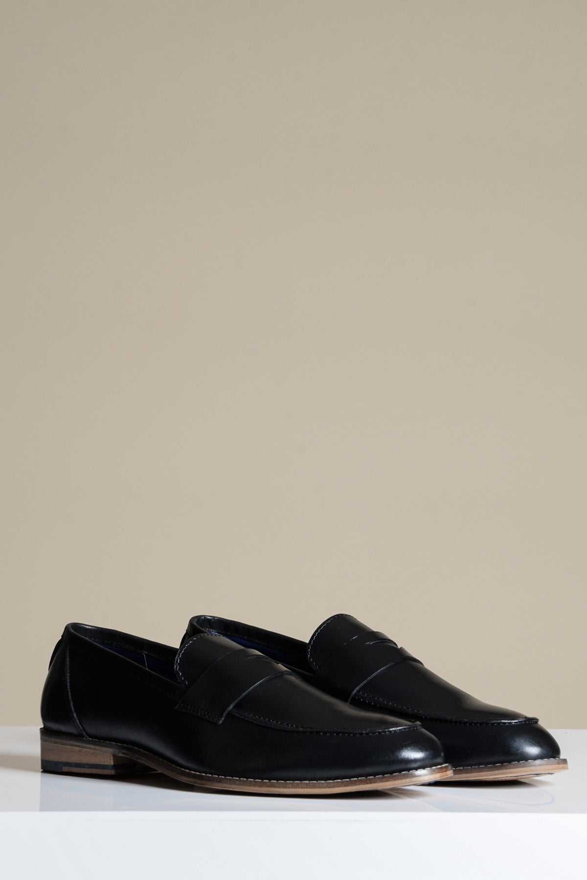 The JASPER Black Leather Penny Loafer Shoe by Marc Darcy features low wooden heels and is displayed on a white surface with a plain beige background.