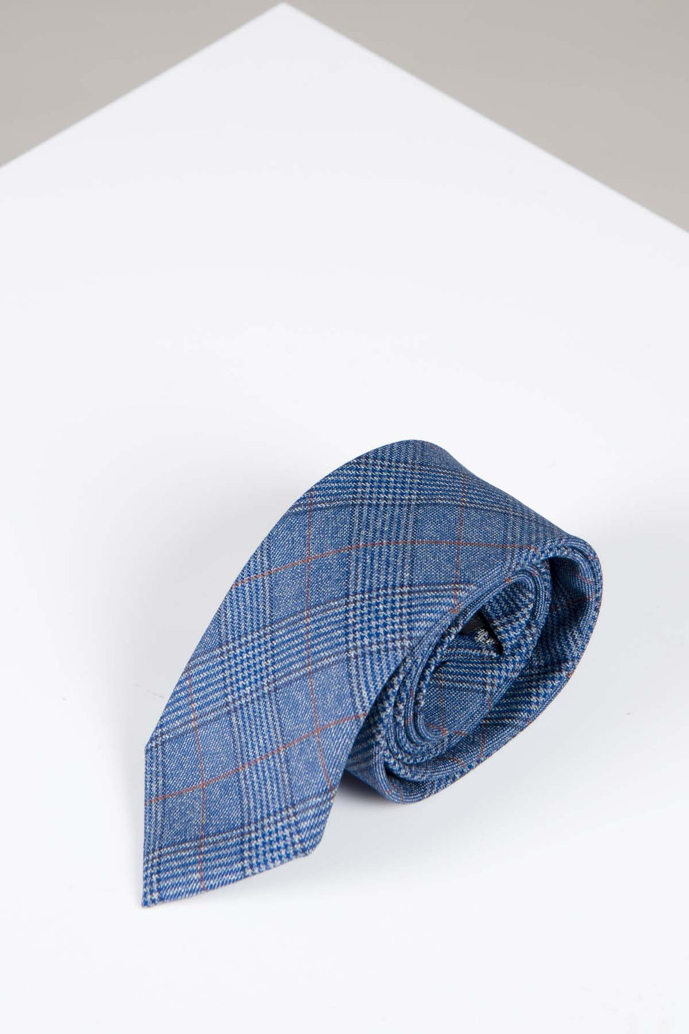 The GEORGE - Light Blue Check Tie by Accessory features a subtle red and gray Prince of Wales pattern, neatly rolled and displayed on a white, angular surface.