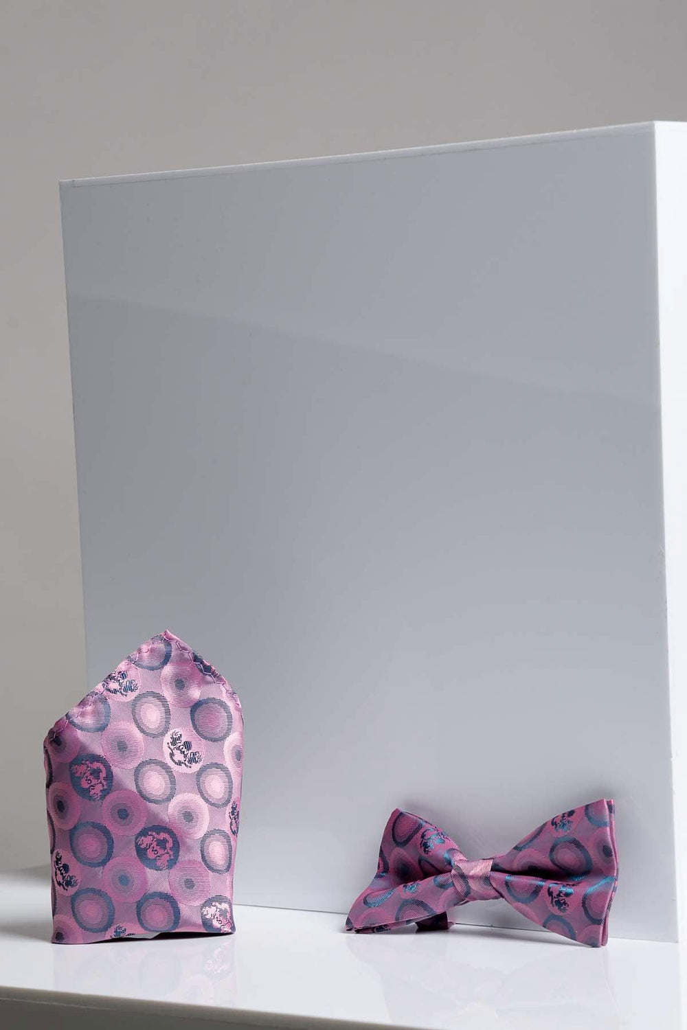 The Marc Darcy BUBBLES - Baby Pink Bubble Circle Print Bow Tie and Pocket Square Set is shown pre-tied and neatly arranged on a white surface against a plain background.