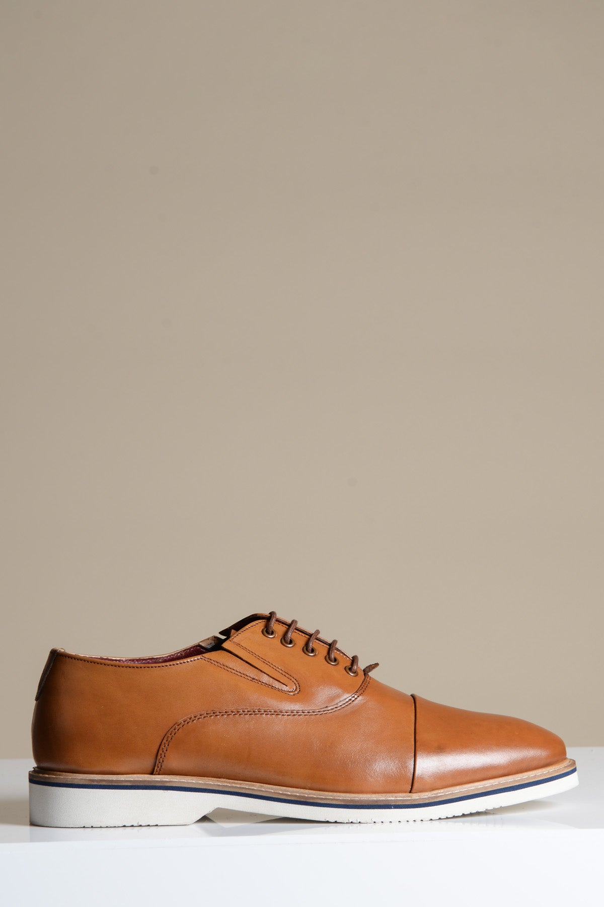 The Marc Darcy GAVIN is a tan leather cap toe oxford shoe, crafted from full grain leather with a white rubber sole and blue trim—ideal for anyone after formal footwear with a modern touch.