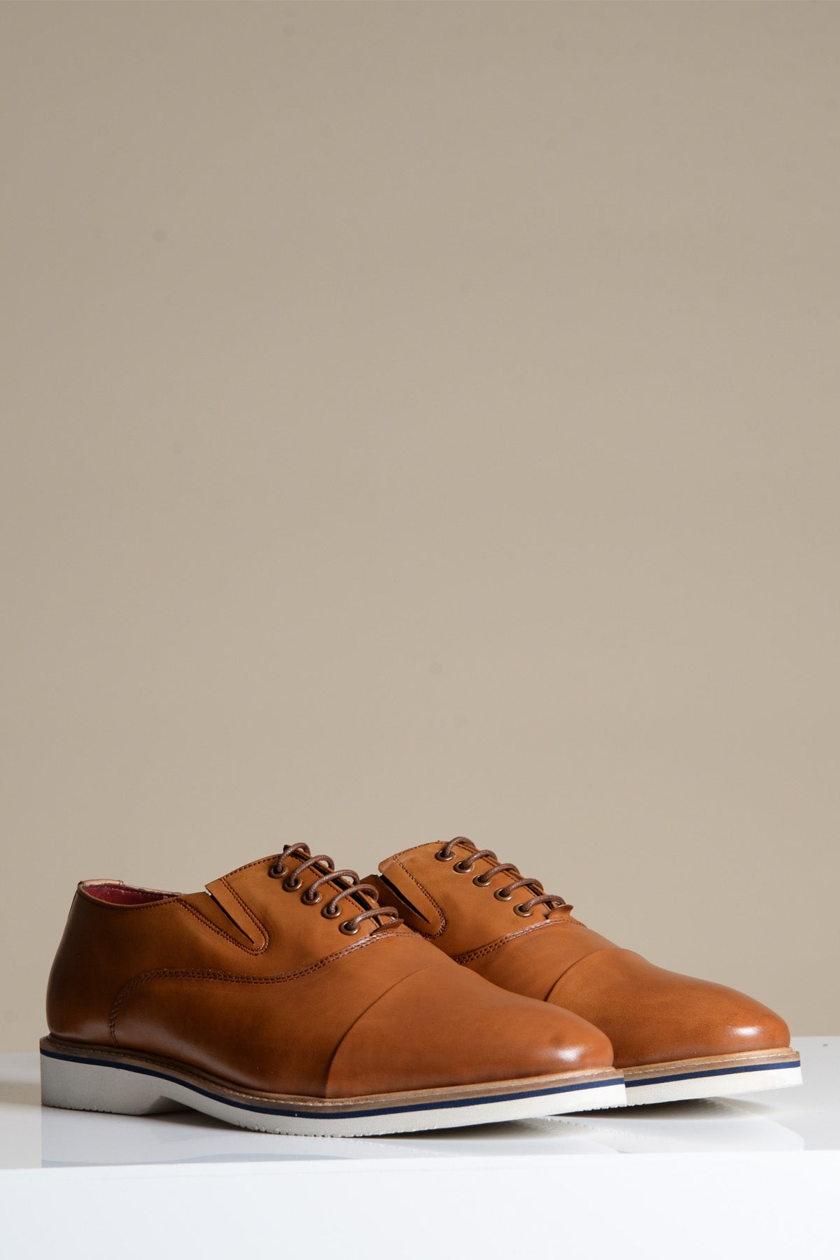 The Marc Darcy GAVIN Tan Leather Cap Toe Oxford Shoe is shown with white soles on a white surface, set against a neutral beige background.
