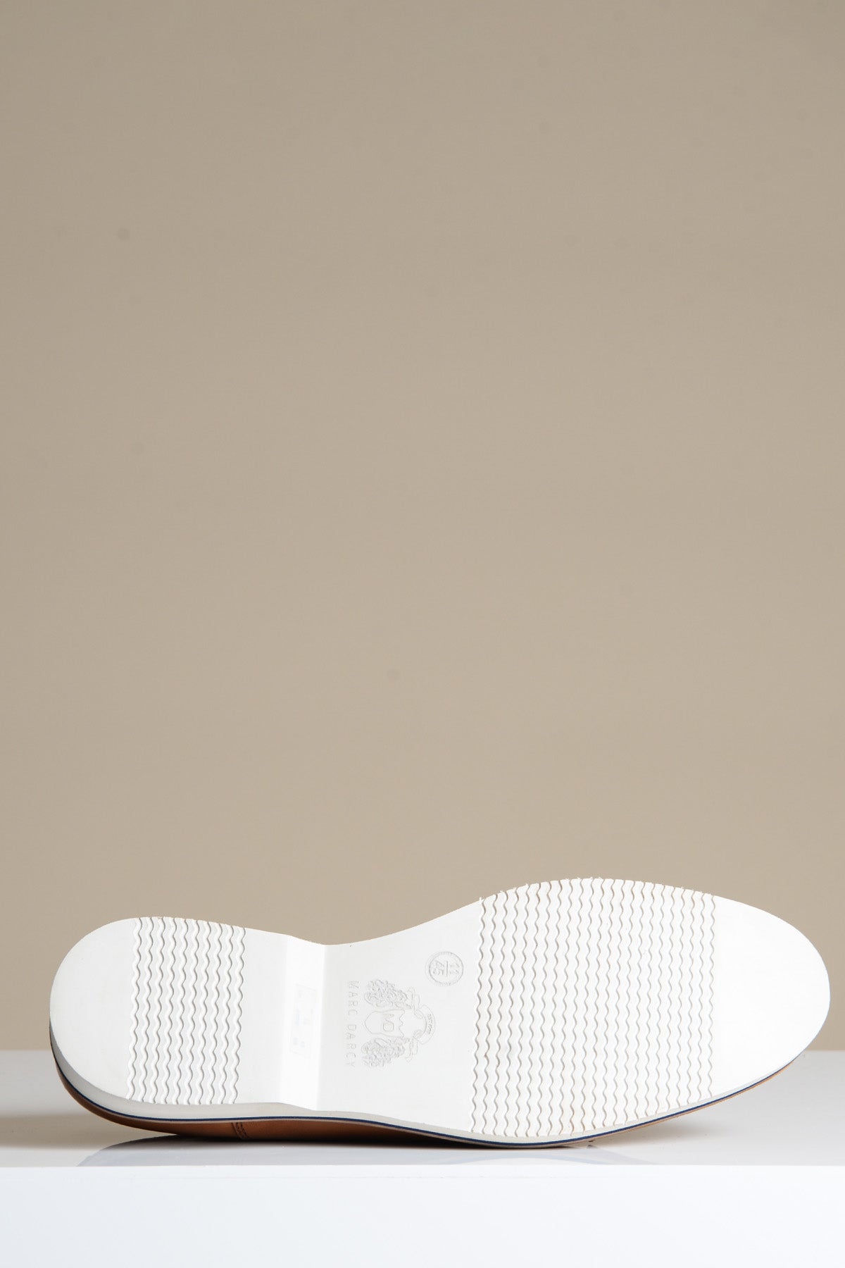 A close-up of the white sole of the GAVIN - Tan Leather Cap Toe Oxford Shoe by Marc Darcy, displayed horizontally on a reflective white surface against a plain beige background.