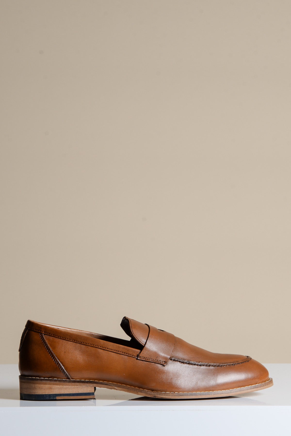 A single JASPER Tan Leather Penny Loafer Shoe by Marc Darcy is displayed on a white surface against a beige background.