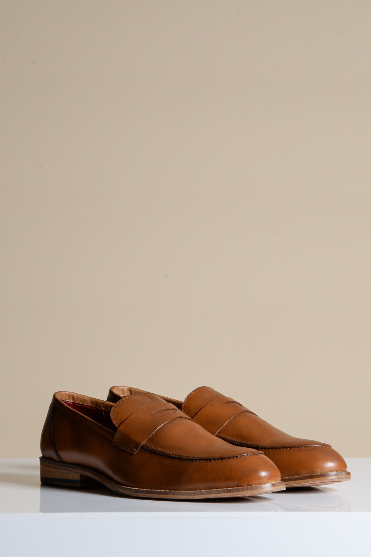 The JASPER Tan Leather Penny Loafer Shoe by Marc Darcy, featuring hand-stitched detailing and a classic design, is displayed side by side on a white surface with a plain beige background.
