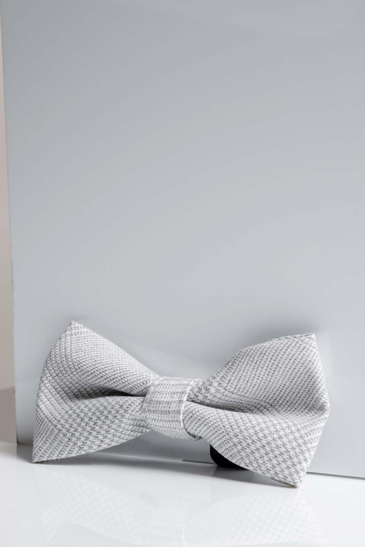 The Accessory BROMLEY - Stone Check Bow Tie, featuring a textured light gray check pattern, is shown against a plain background with soft lighting accentuating its elegant details—ideal for formal occasions.