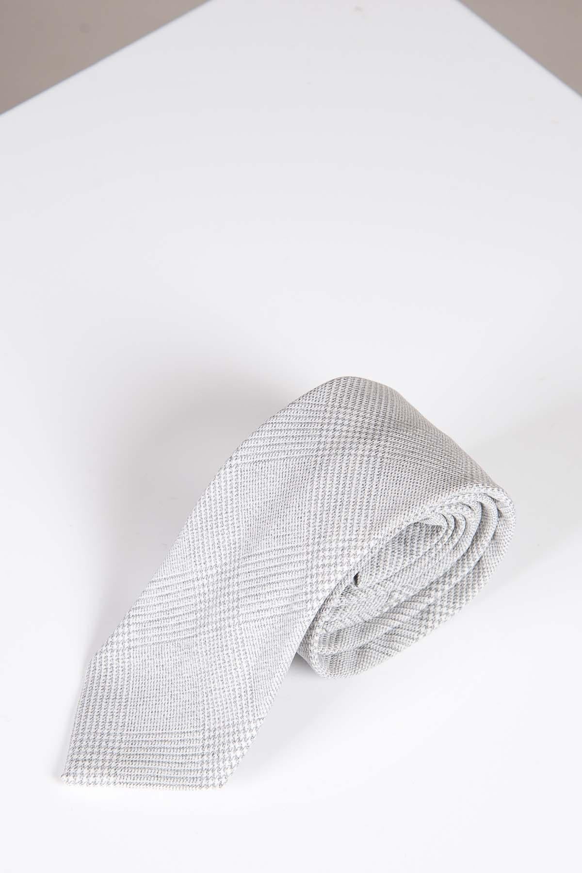 The BROMLEY - Stone Check Tie by Accessory is rolled up on a white surface with a hint of beige background, highlighting its classic Prince of Wales pattern.