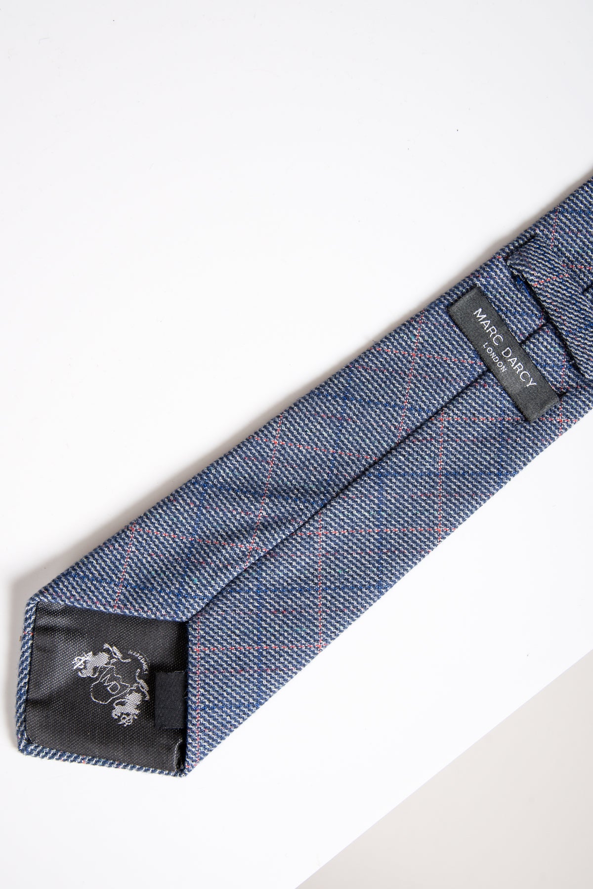 A close-up of the HILTON - Blue Check Tweed Tie by Accessory, featuring a pink and blue check pattern with thin red lines and branded labels on the underside.