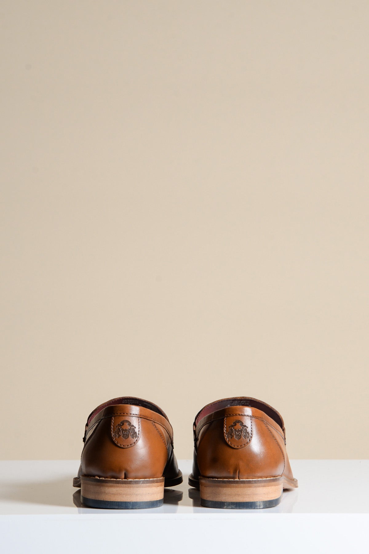 Back view of two JASPER tan leather penny loafer shoes by Marc Darcy, hand-stitched, set against a tan background.