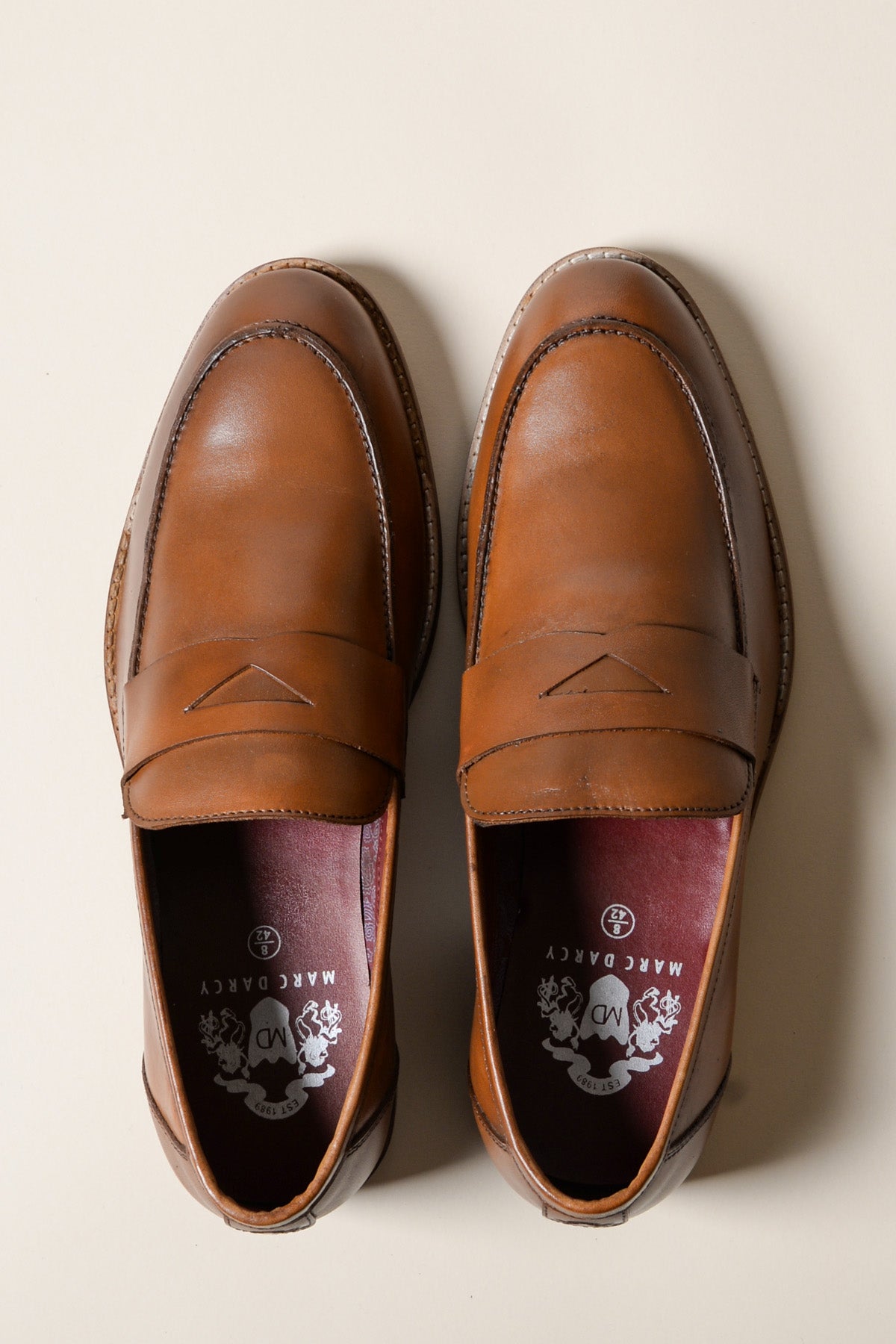 The JASPER Tan Leather Penny Loafer Shoe by Marc Darcy features a penny strap and full grain leather, shown from above on a neutral background. The insoles display decorative Marc Darcy branding.