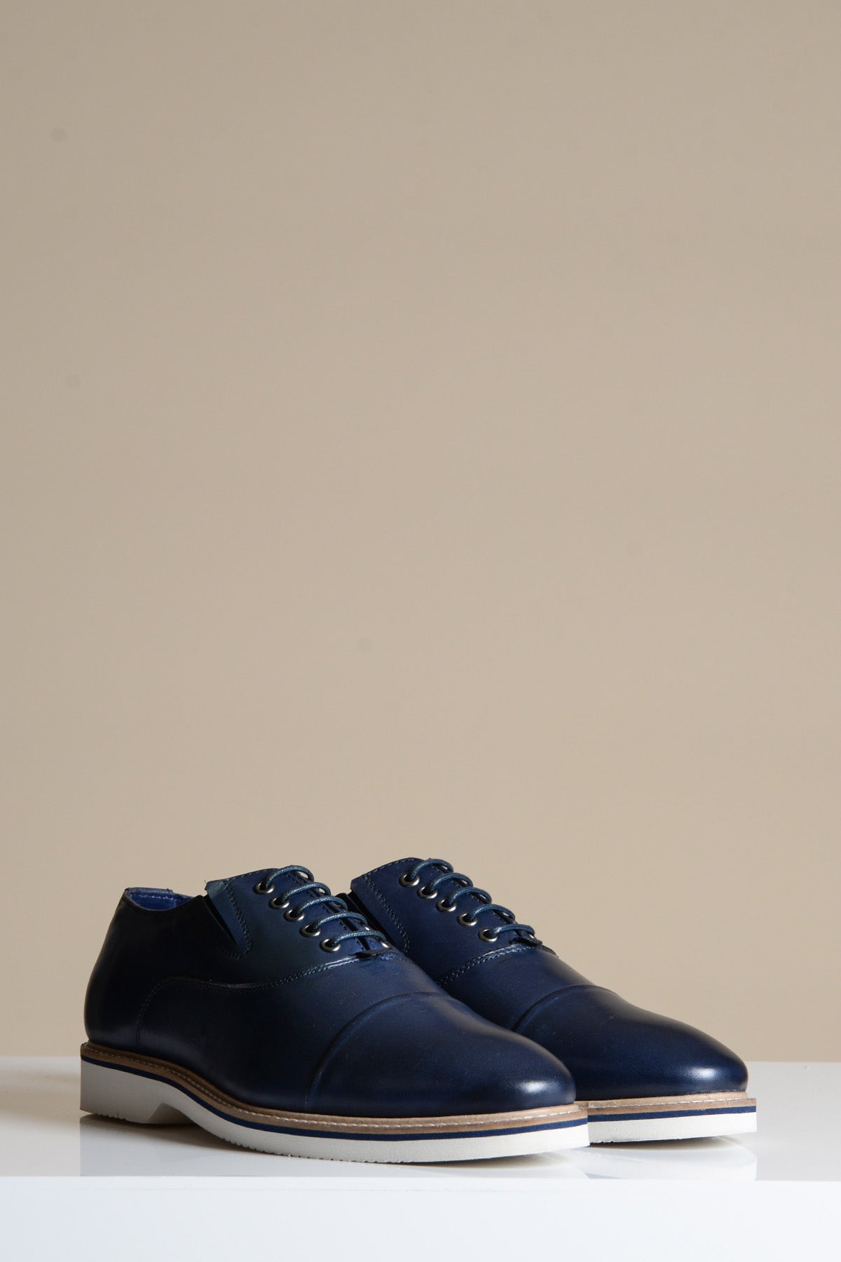 The Marc Darcy GAVIN Navy Blue Leather Cap Toe Oxford Shoe features full grain leather, white soles, and black laces, displayed on a white surface with a plain beige background.