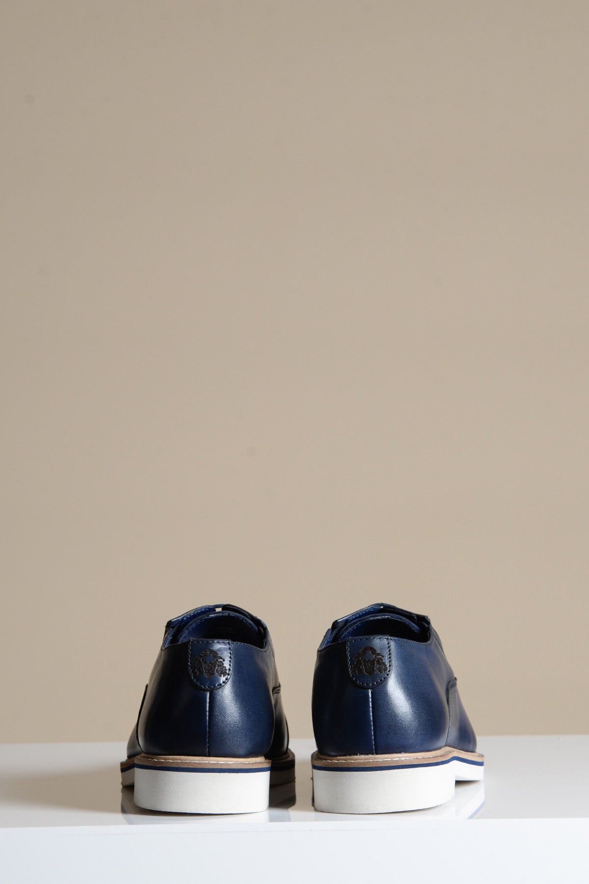 The Marc Darcy GAVIN Navy Blue Leather Cap Toe Oxford Shoes, crafted from full grain leather with white soles, are shown from the back on a white surface against a plain beige background.