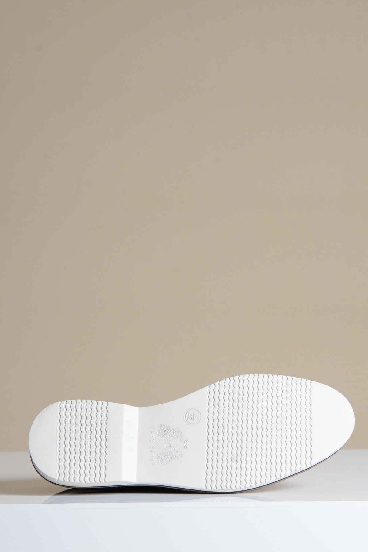 The white rubber sole of the Marc Darcy GAVIN - Navy Blue Leather Cap Toe Oxford Shoe is shown facing up on a beige and white background, displaying its textured grip—ideal for pairing with full grain leather footwear.
