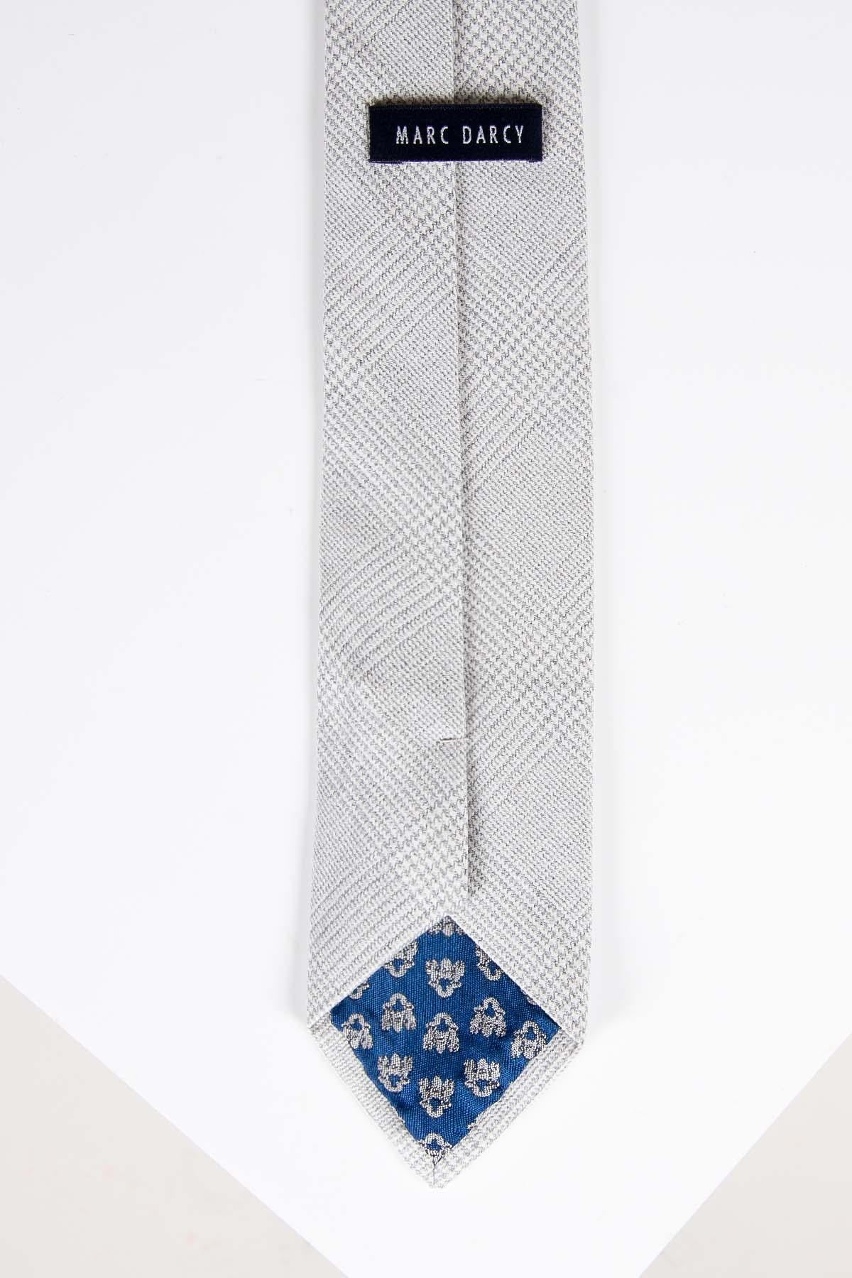 The BROMLEY - Stone Check Tie by Accessory features a light grey textured design with a blue inner tip and white floral pattern, displayed flat on a white background.