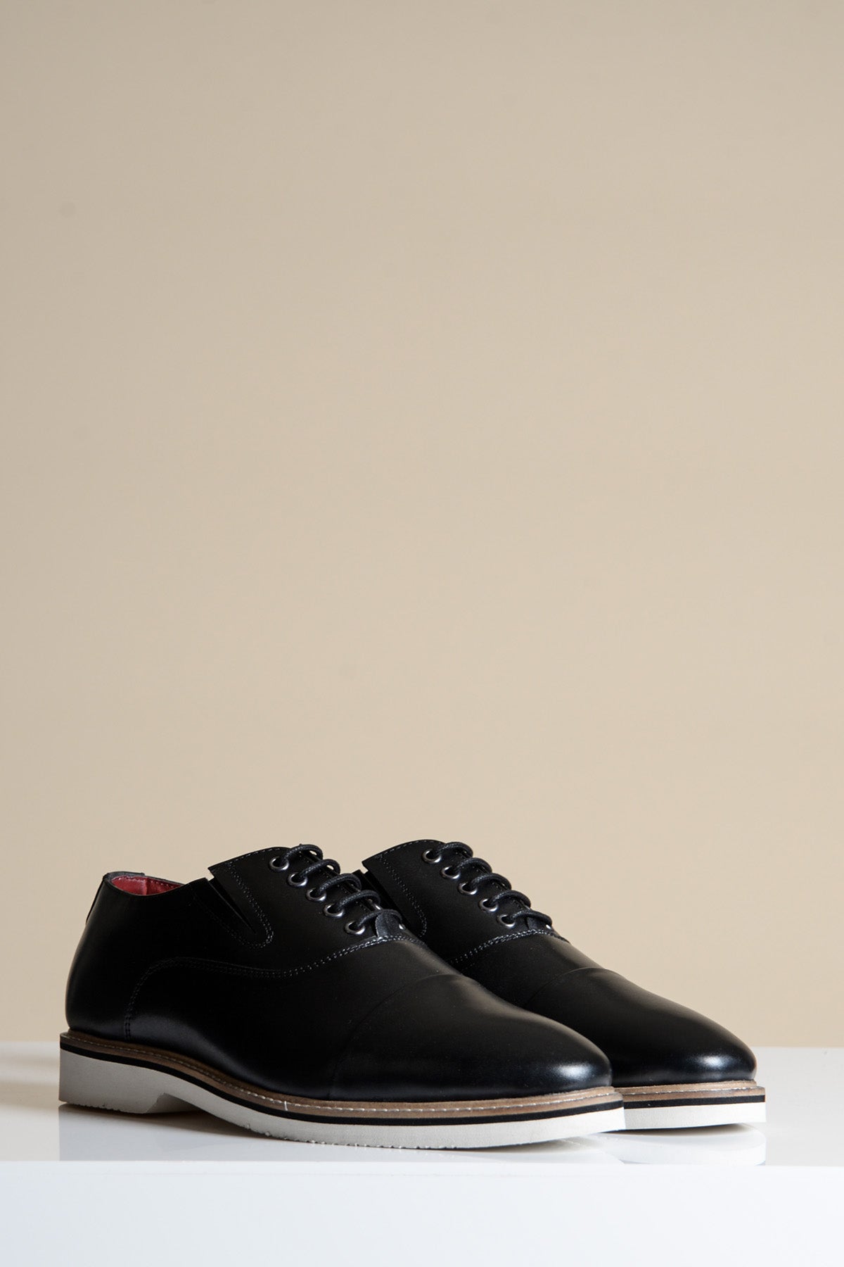 The Marc Darcy GAVIN Black Leather Cap Toe Oxford Shoes feature full grain leather, black laces, and white soles, elegantly displayed on a white surface with a beige background.