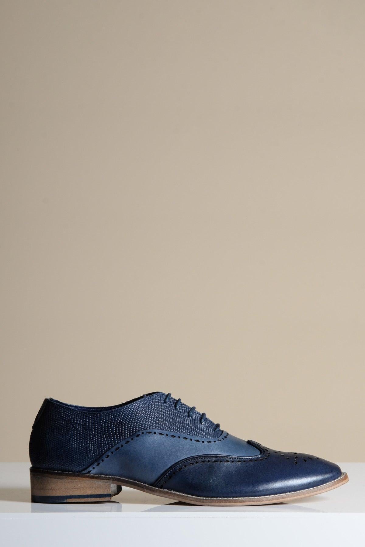 The Marc Darcy RYAN Navy Blue Leather Wingtip Brogue Shoe with a wooden sole is displayed on a white surface against a plain beige background.