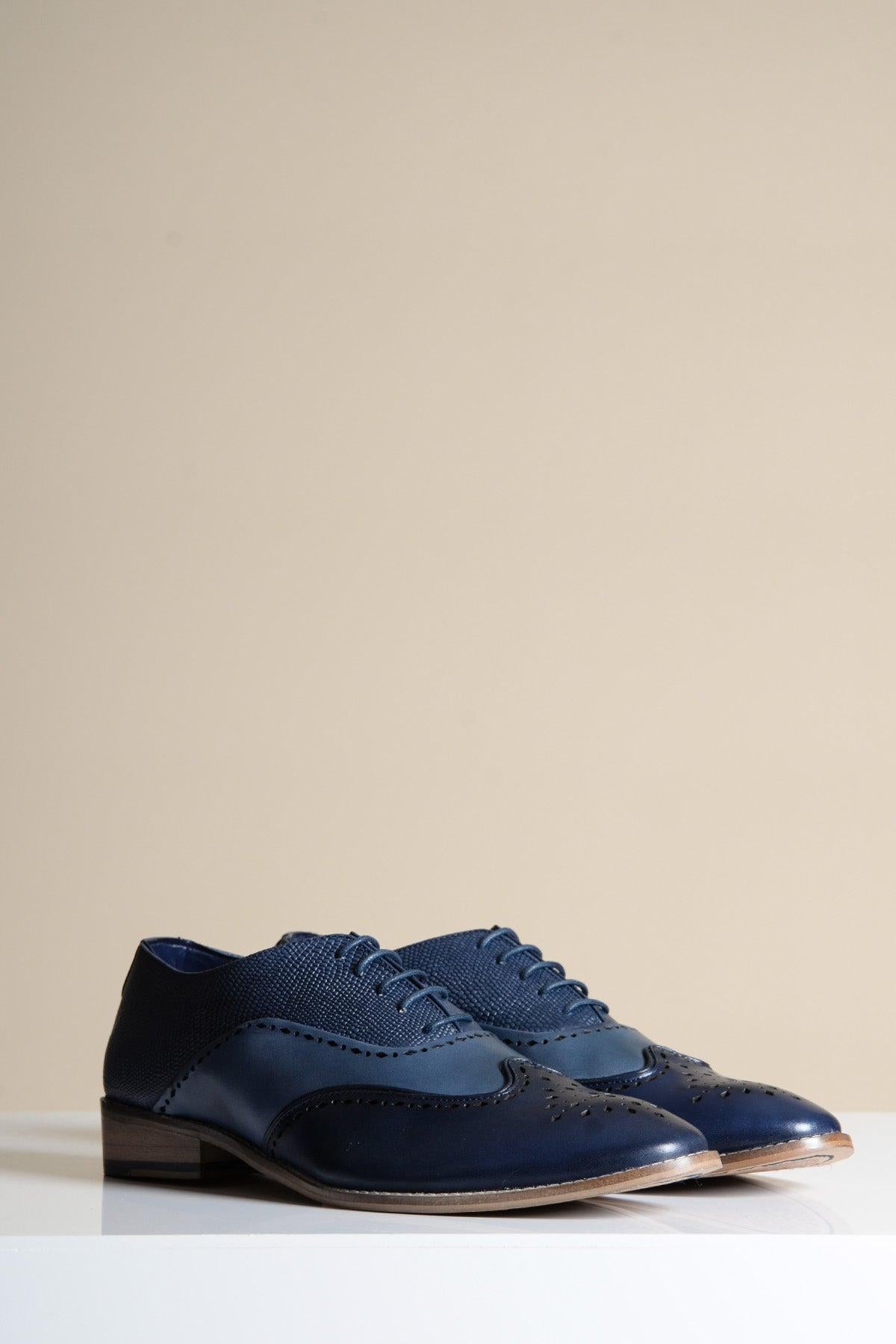 The RYAN Navy Blue Leather Wingtip Brogue Shoes by Marc Darcy showcase classic brogue detailing and wooden soles, elegantly displayed on a white surface with a plain beige background.