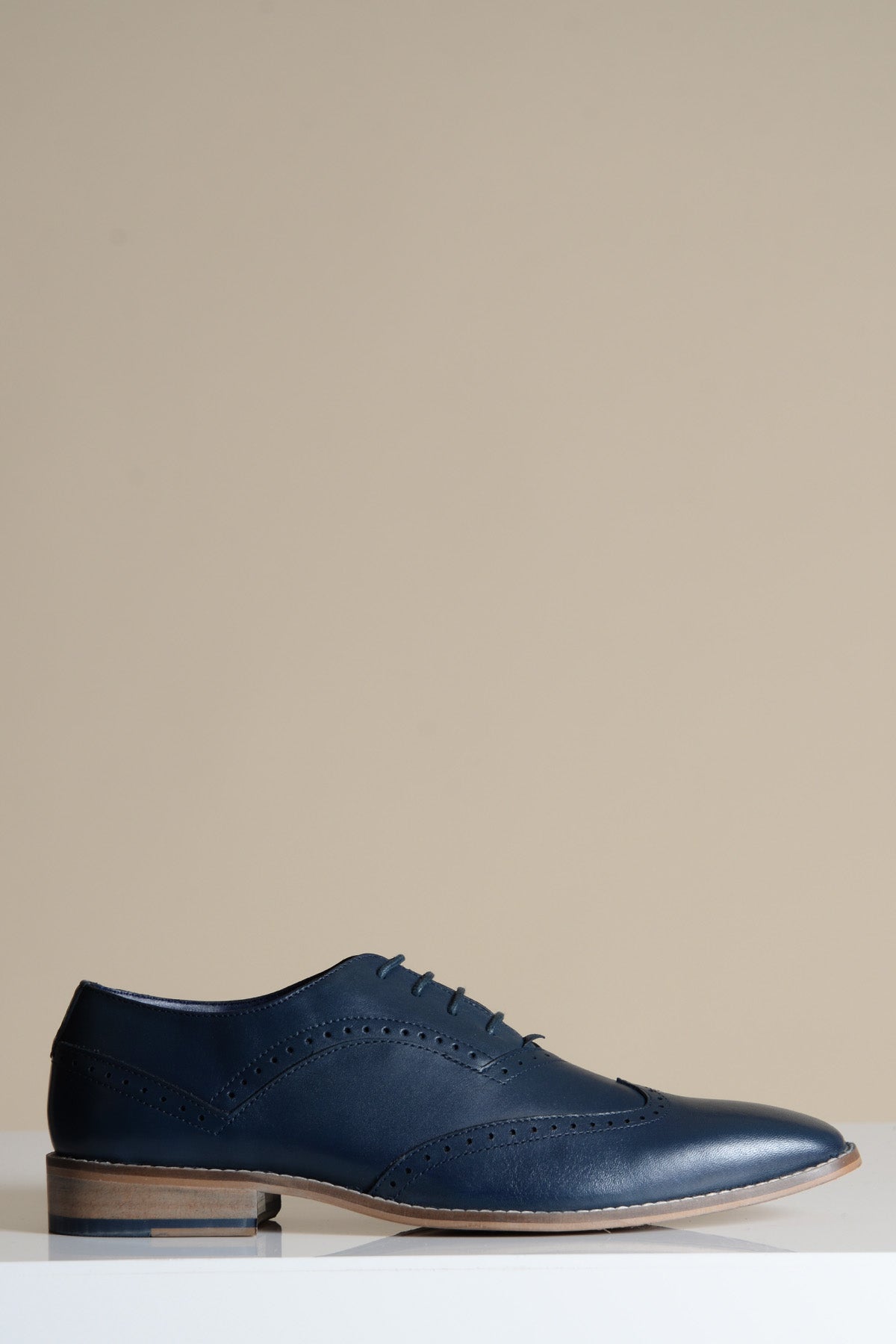 The Marc Darcy DAWSON Navy Wingtip Oxford Brogue Shoe features full grain leather, classic brogue detailing, and a light brown sole, shown against a beige background.