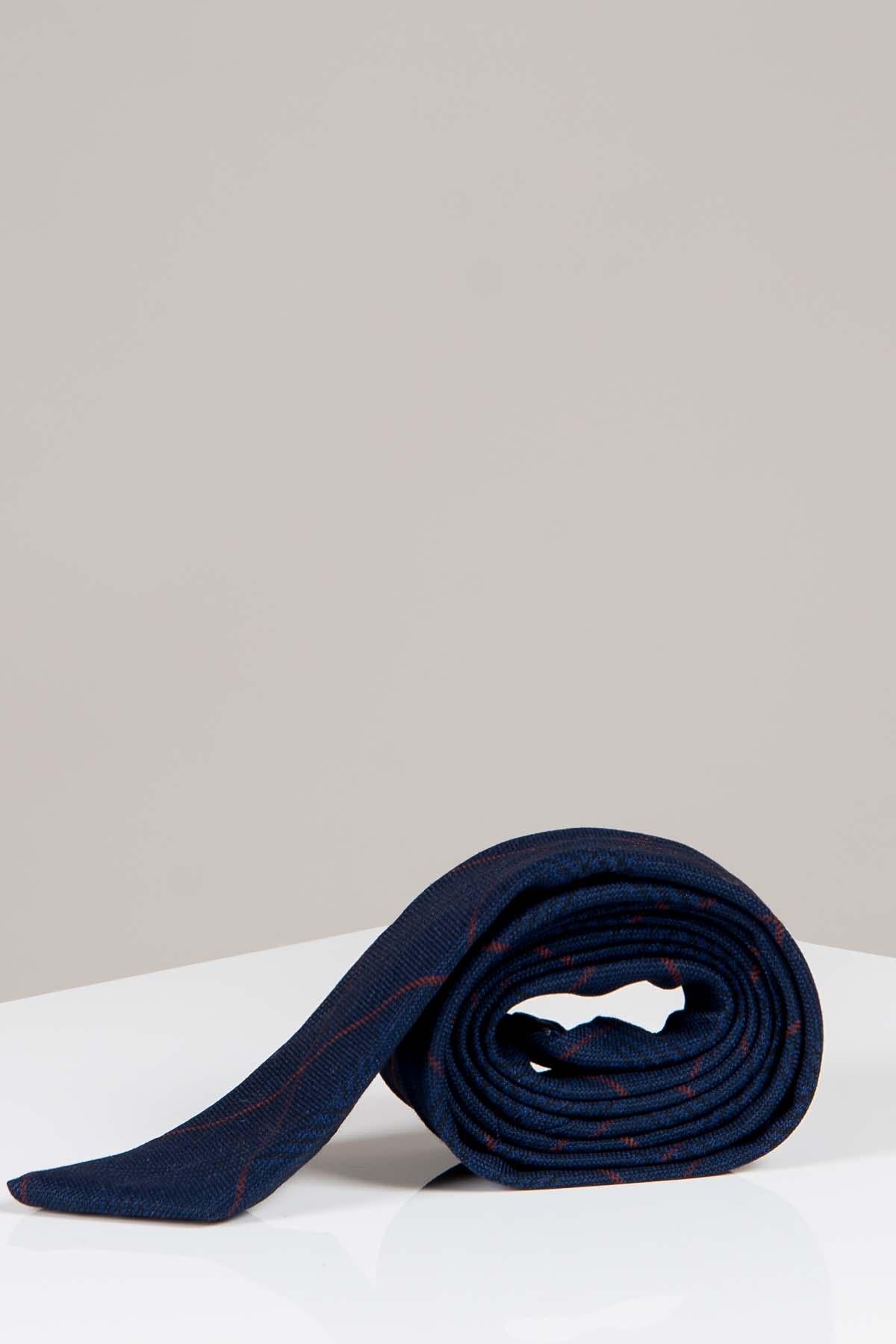 The EDINSON - Navy Wine Check Tie by Accessory is a handmade men's tie with a navy base and subtle red plaid pattern, offering a classic look. Shown rolled on a white surface with a light grey background.