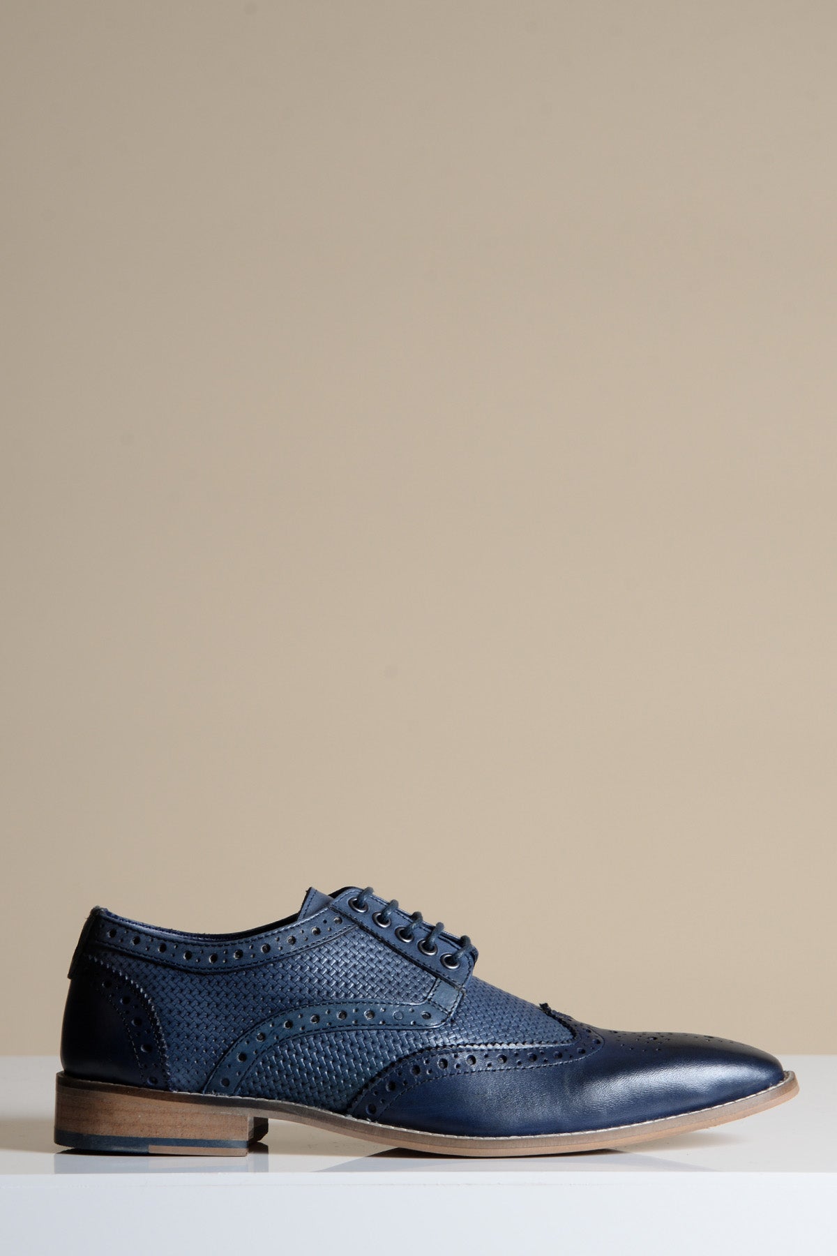 The marcdarcy BRANDON Navy Blue Leather Wingtip Brogue Shoe, featuring hand-crafted perforated detailing and a light brown sole, is displayed against a plain beige background.