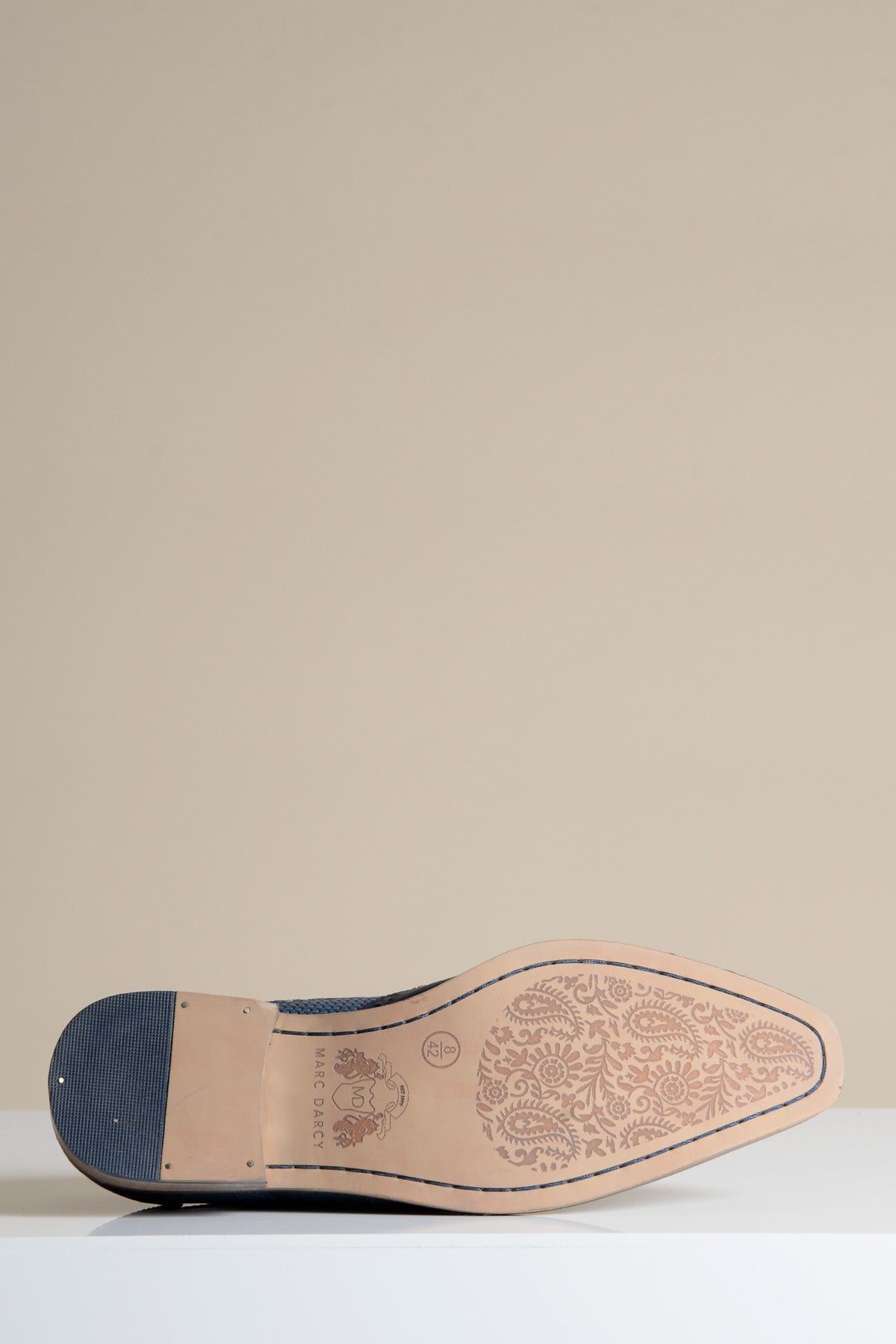 A close-up of the sole on the marcdarcy BRANDON Navy Blue Leather Wingtip Brogue Shoe showcases hand-crafted floral engravings on the light tan base, paired with a premium navy leather upper against a neutral background.