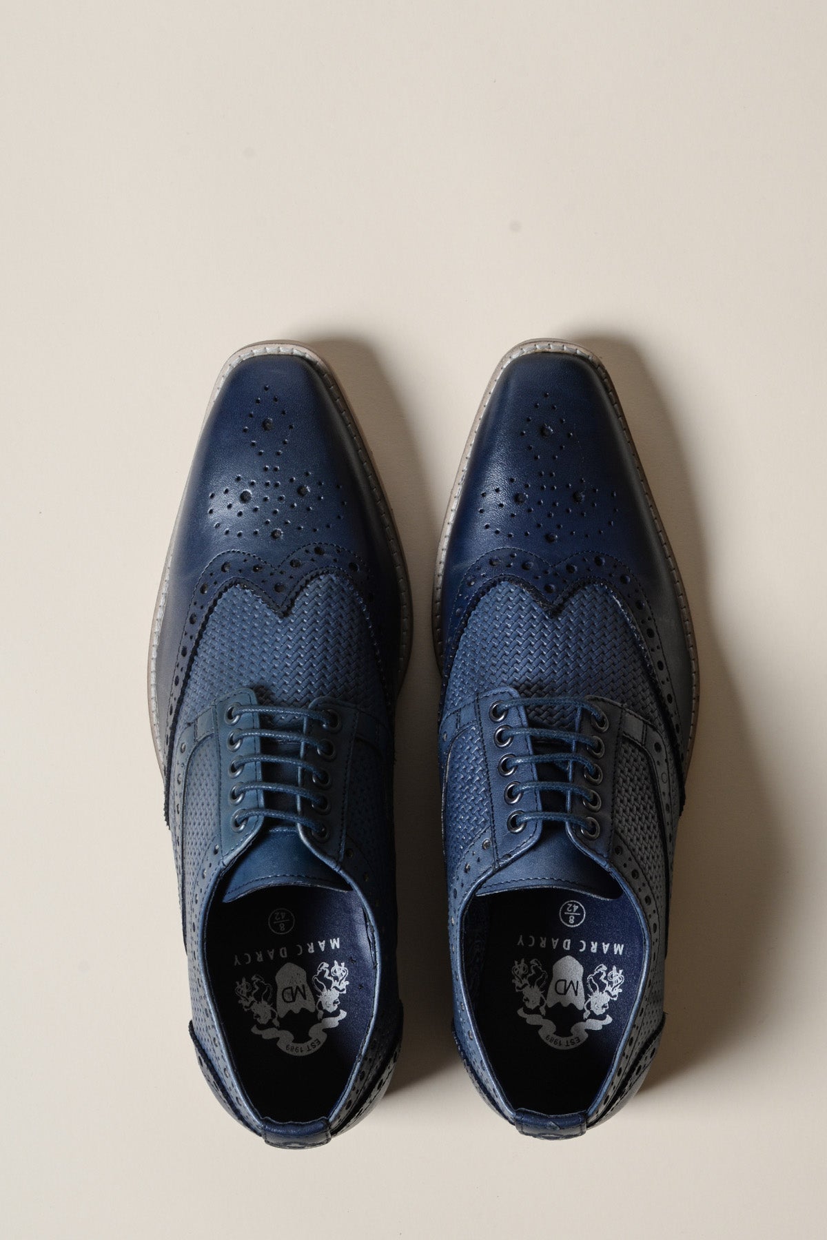 The marcdarcy BRANDON Navy Blue Leather Wingtip Brogue Shoes, featuring hand-crafted perforations, laces, and visible branding, are displayed side by side on a light beige surface.
