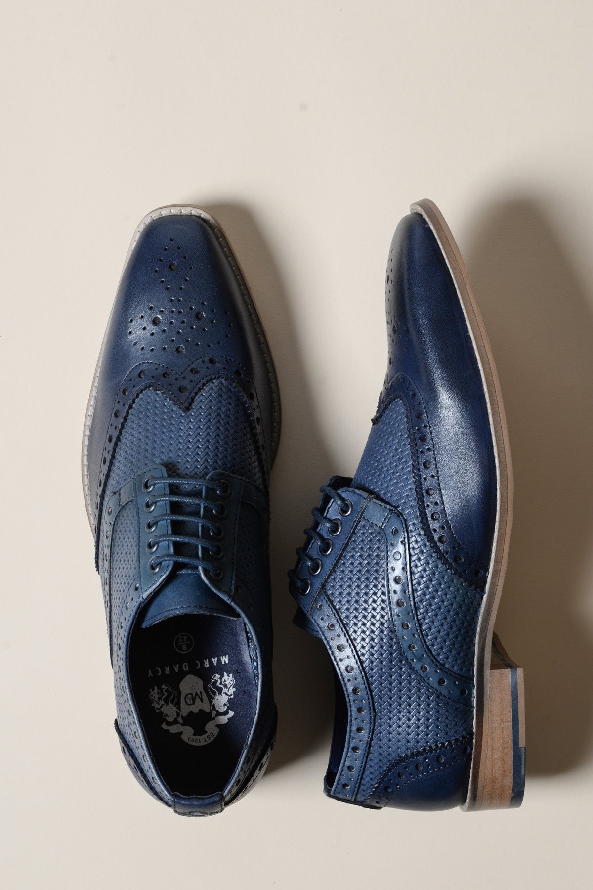 The marcdarcy BRANDON Navy Blue Leather Wingtip Brogue Shoe features hand-crafted detailing, laces, light brown soles, and a cushioned insole, displayed on a light beige background.