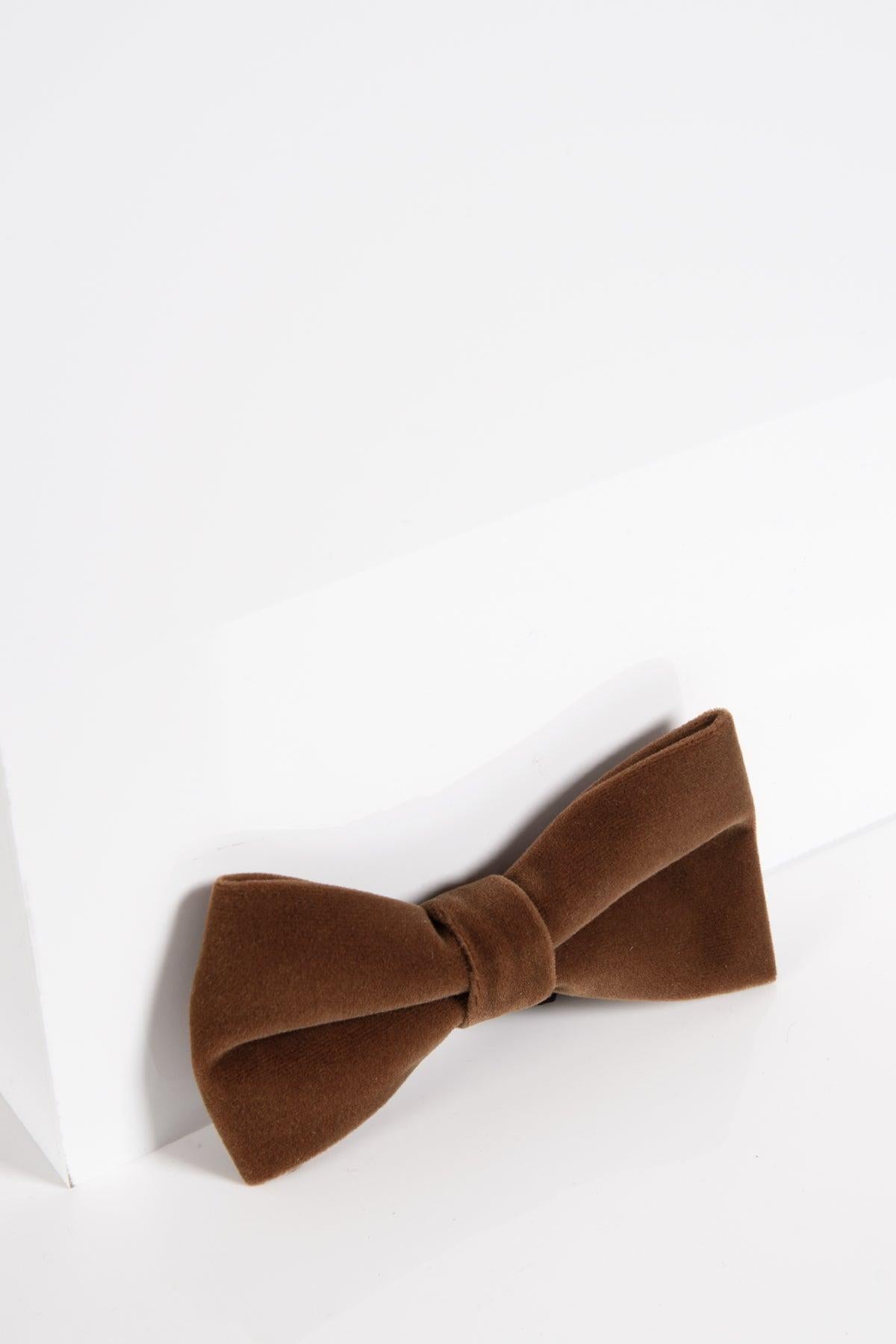 The VELVET - Dark Tan Velvet Bow Tie by Accessory is a handmade brown velvet bow tie, displayed on a white surface with a geometric accent—ideal for anyone seeking a distinctive look at black tie events.