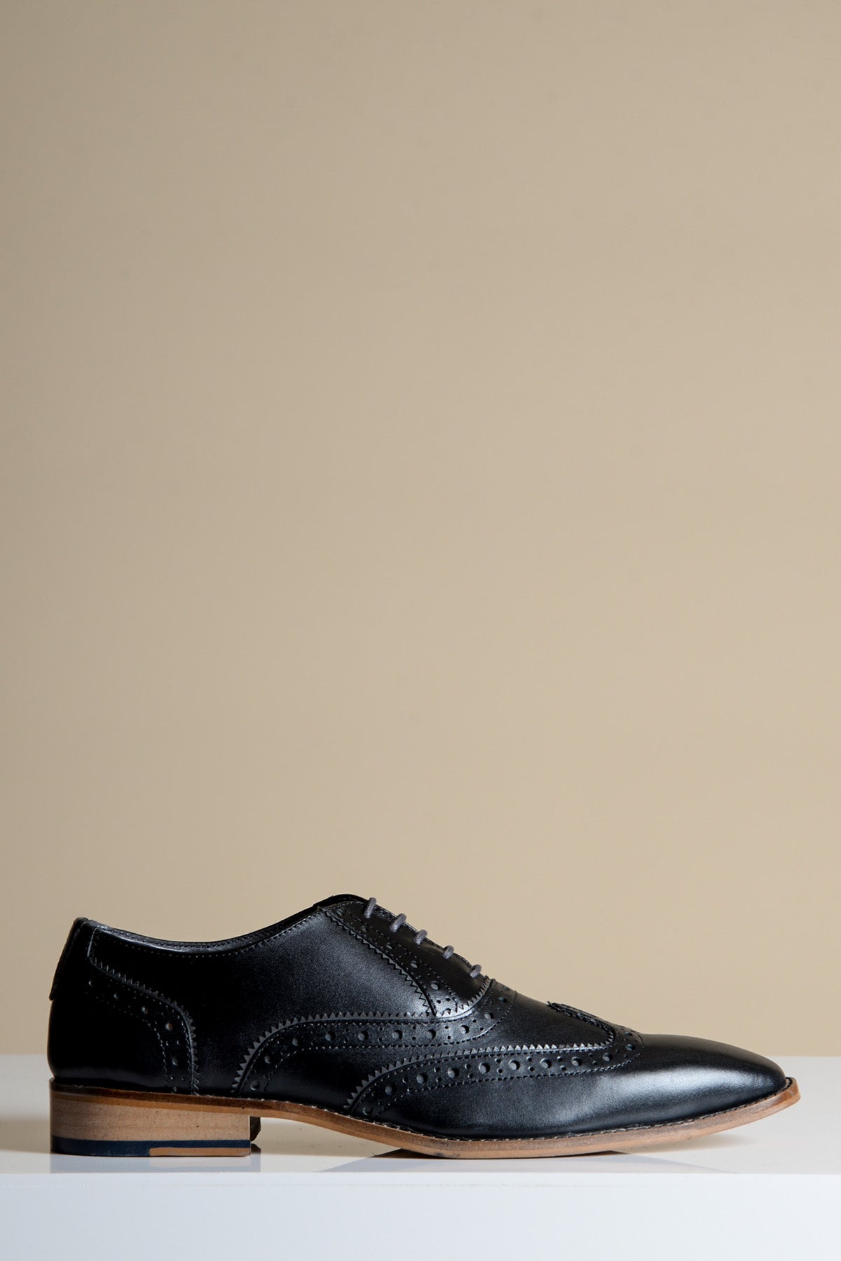 The MARCO - Black Grey Leather Wingtip Oxford Shoe by Marc Darcy, crafted from full grain leather with brogue detailing and a light brown sole, is displayed against a plain beige background.