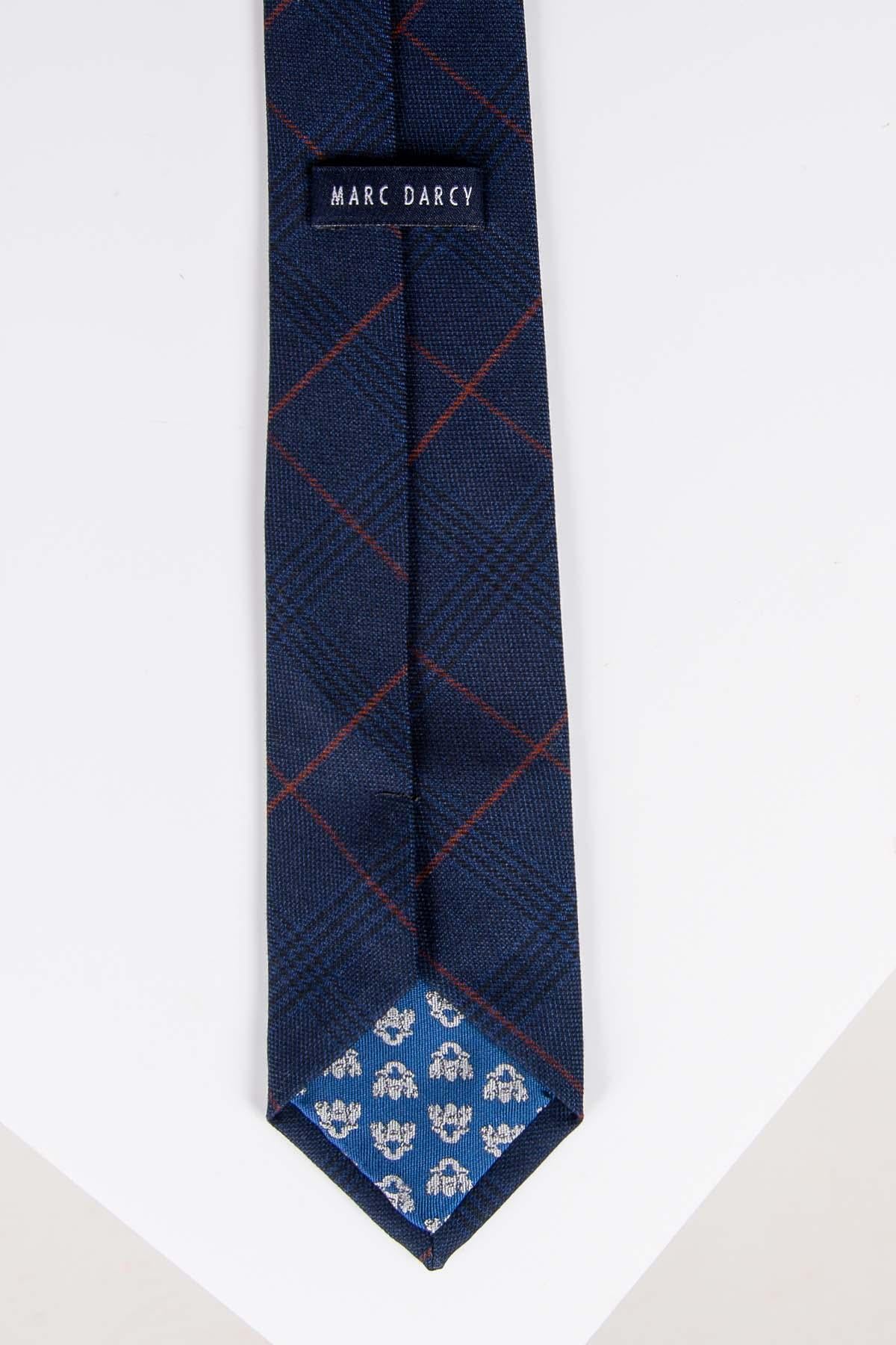 The EDINSON - Navy Wine Check Tie by Accessory is a handmade mens tie featuring a navy base with a red check pattern. The underside of the tip showcases blue fabric with a small white floral motif, and it is displayed flat on a white surface.