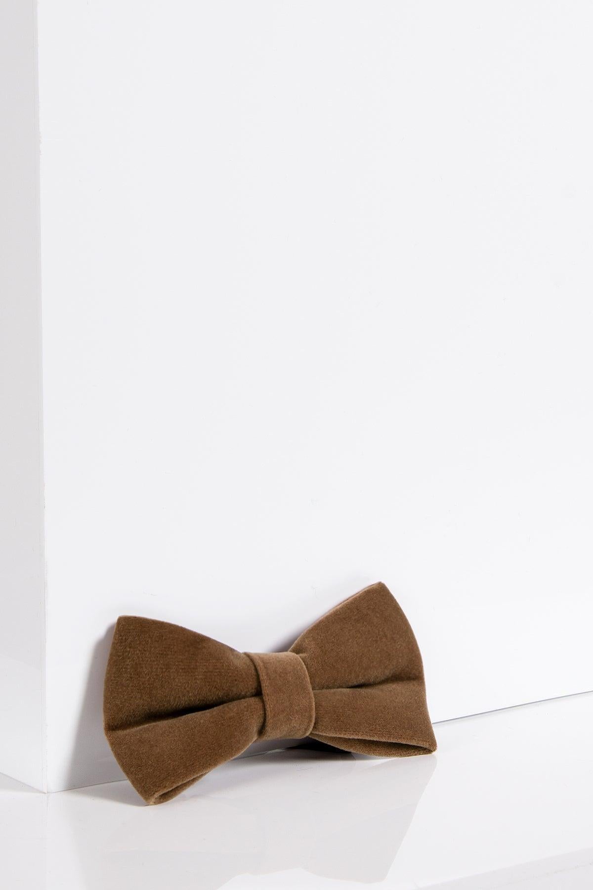 The VELVET - Light Tan Velvet Bow Tie by Accessory sits on a glossy white surface with a minimal background—an elegant, refined piece for any accessory collection.