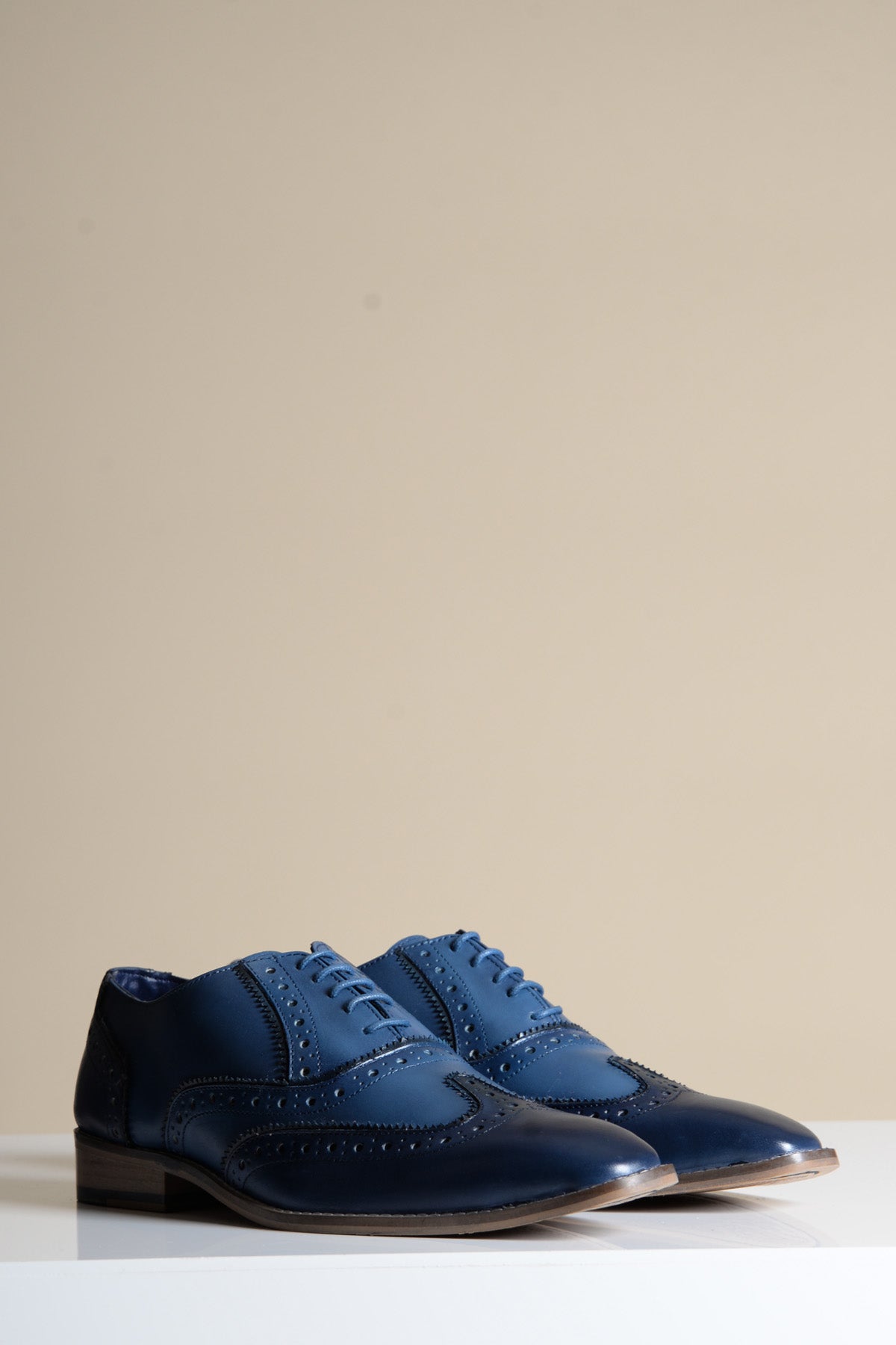 The MARCO Navy Blue Leather Wingtip Oxford Shoe by Marc Darcy, crafted from full grain leather with hand-stitched detailing, is displayed on a white surface against a plain beige background.