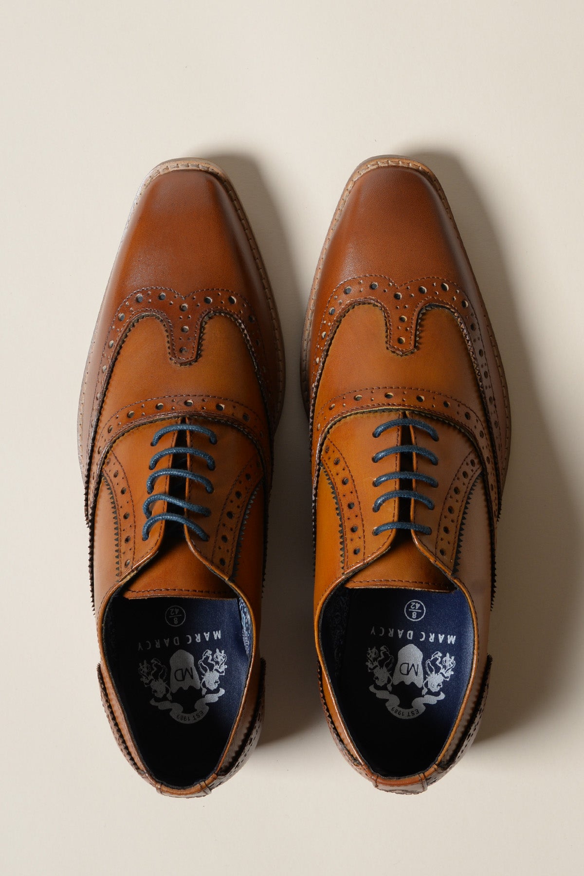 The MARCO - Tan Navy Leather Wingtip Oxford Shoe by Marc Darcy, crafted from leather with brogue and hand-stitched details, dark laces, is shown from above on a light beige background.