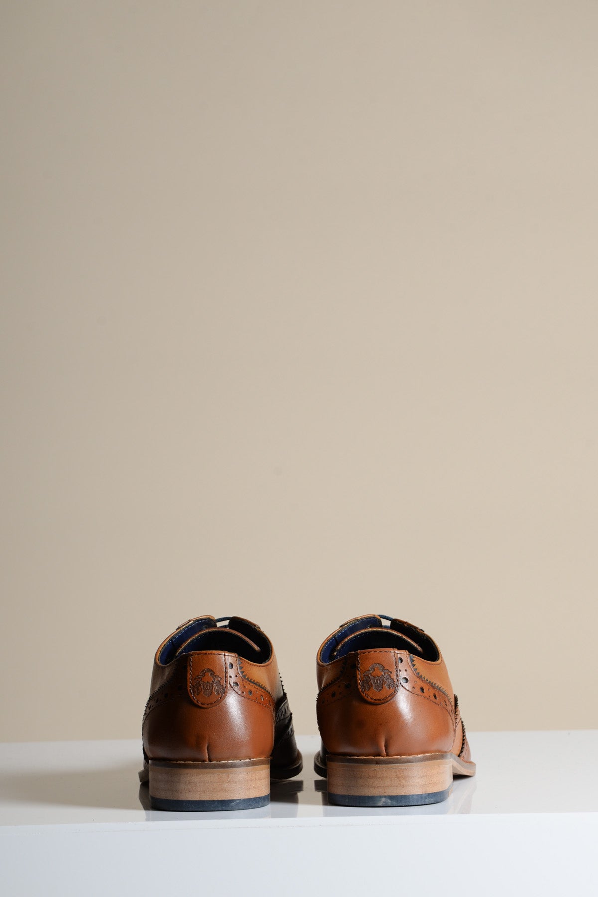 The MARCO - Tan Navy Leather Wingtip Oxford Shoes by Marc Darcy are placed side by side, facing away on a white surface with a plain beige background.