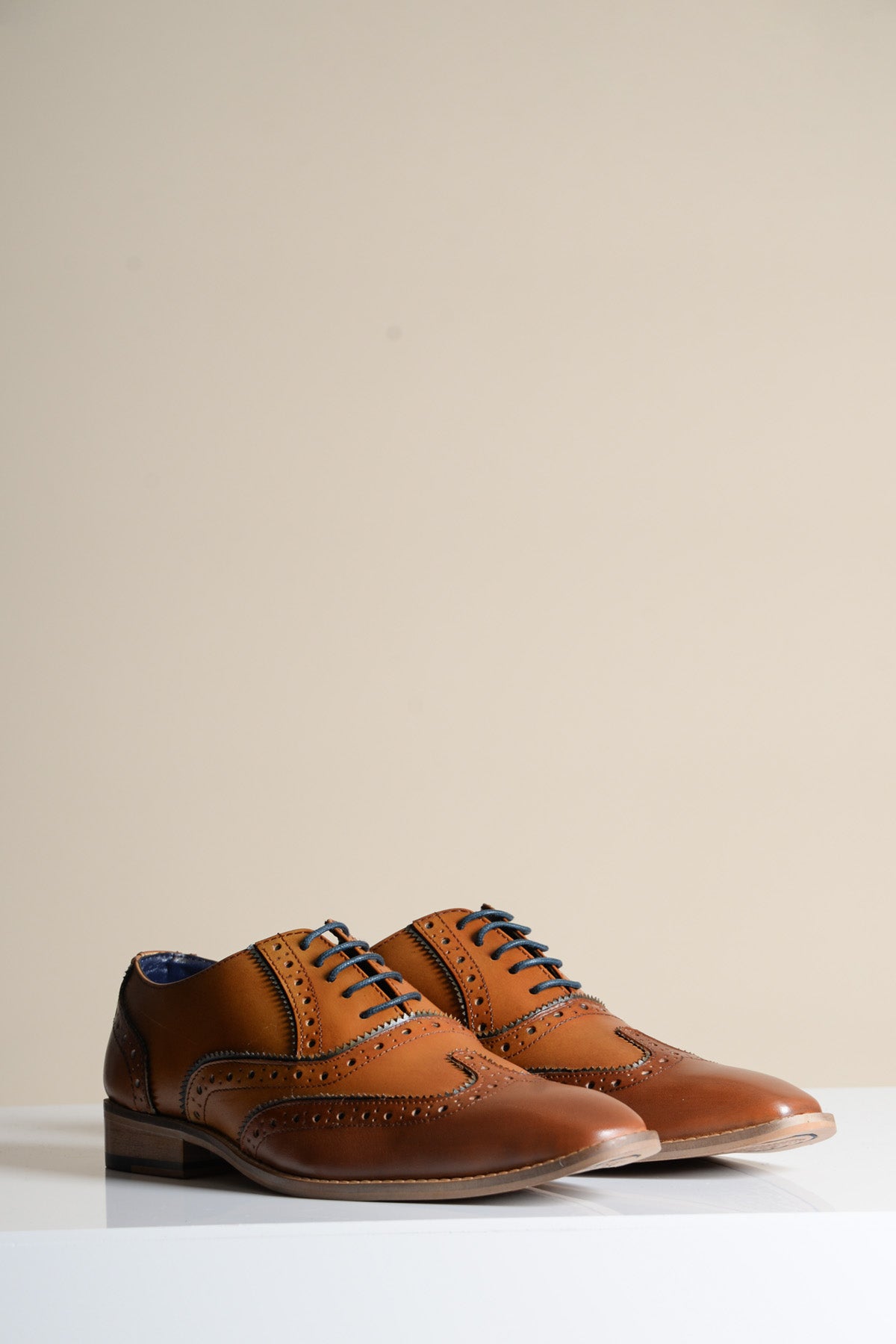 The MARCO - Tan Navy Leather Wingtip Oxford Shoe by Marc Darcy features decorative perforations, black laces, hand-stitched details, and a low heel, displayed on a white surface against a plain beige background.