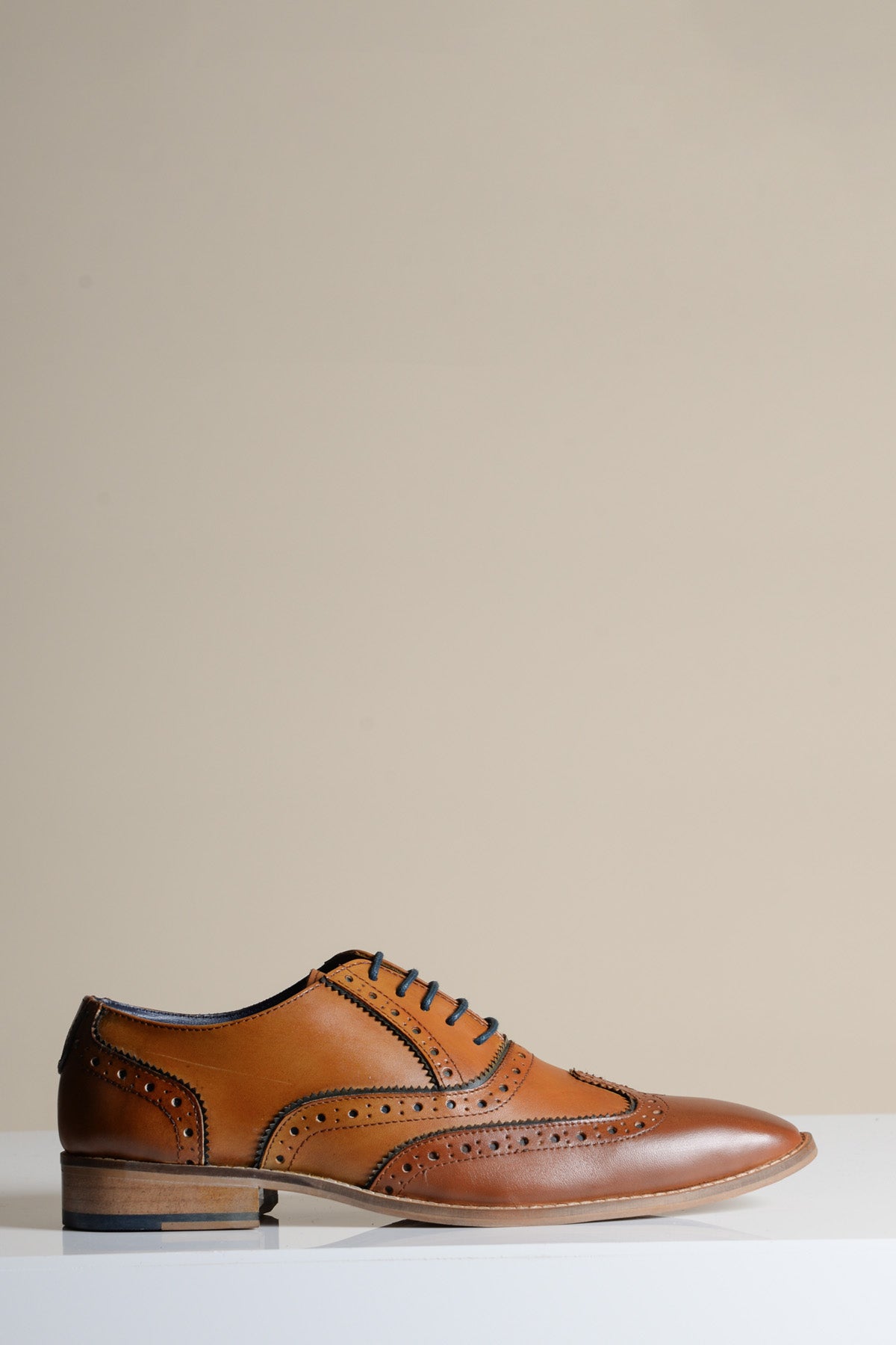 The MARCO - Tan Navy Leather Wingtip Oxford Shoe by Marc Darcy, featuring full grain leather, black laces, and decorative perforations, is shown on a white surface with a neutral beige background.