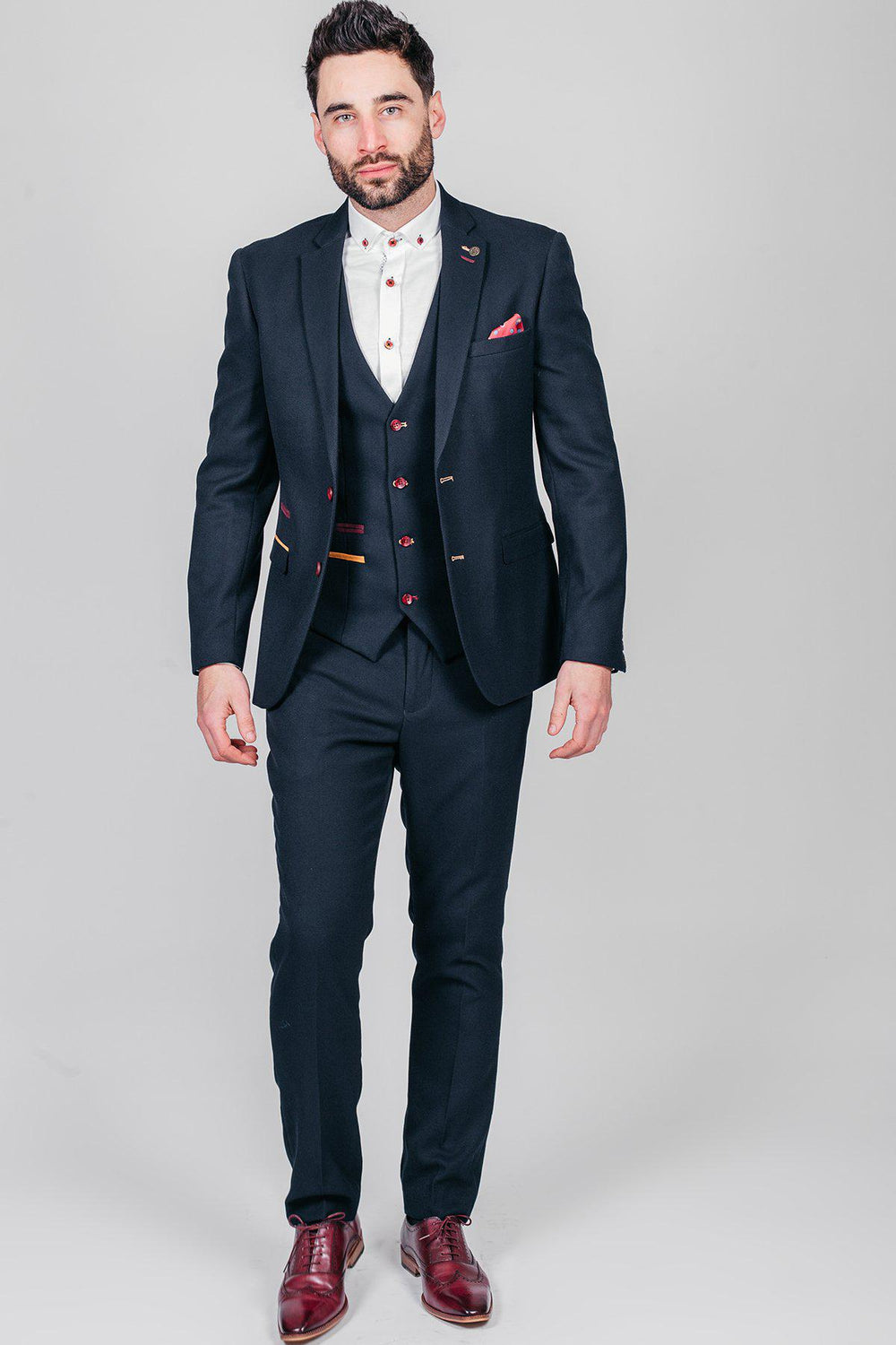 Newcastle United and England goalkeeper Nick Pope wears a marcdarcy JD4 navy suit with a white shirt, vest, burgundy and tan suede shoes, pocket square, red button accents, and paisley lining against a plain light gray background.
