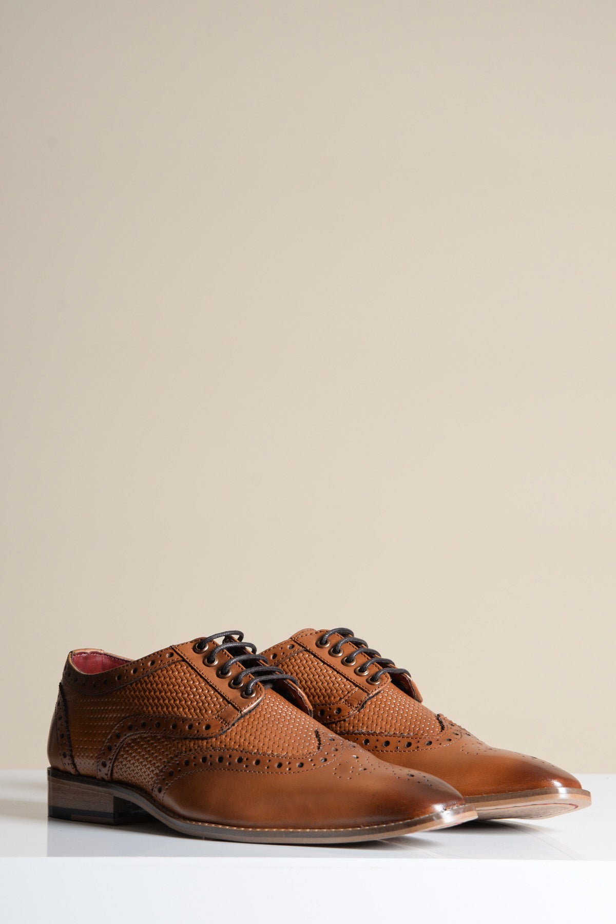 The marcdarcy BRANDON Dark Tan Leather Wingtip Brogue Shoe features hand-stitched detailing, decorative perforations, black laces, and low heels, displayed on a white surface with a beige background.
